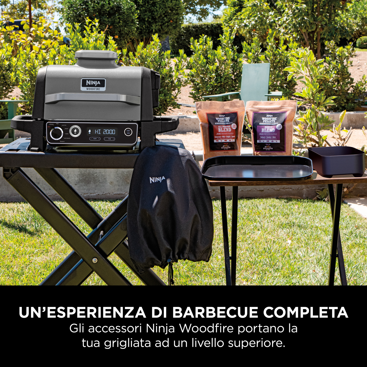 Griglia da esterno Ninja Woodfire su un tavolo, con accessori e sfondo verde.