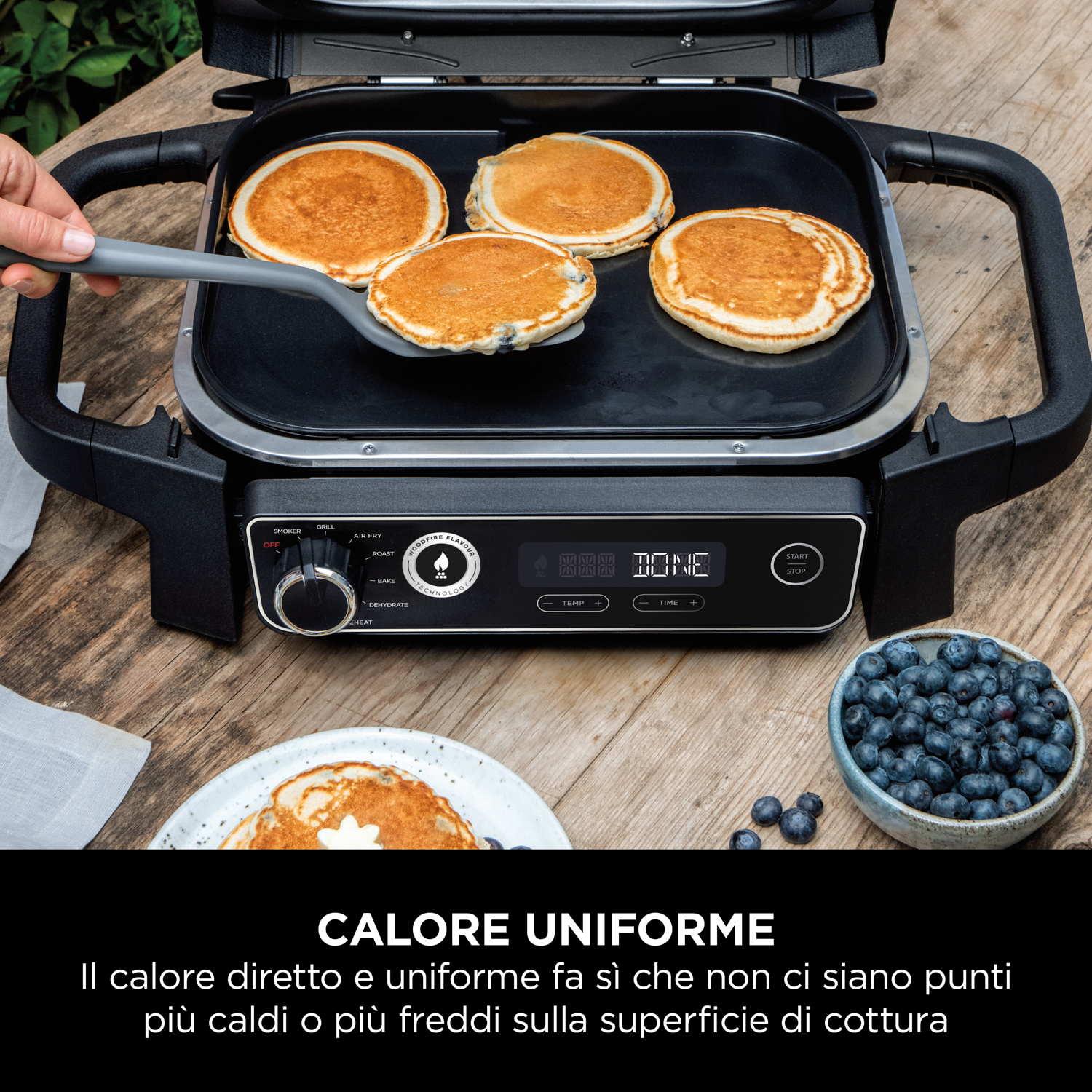 Frittelle in cottura su una griglia elettrica, con una ciotola di mirtilli sullo sfondo.