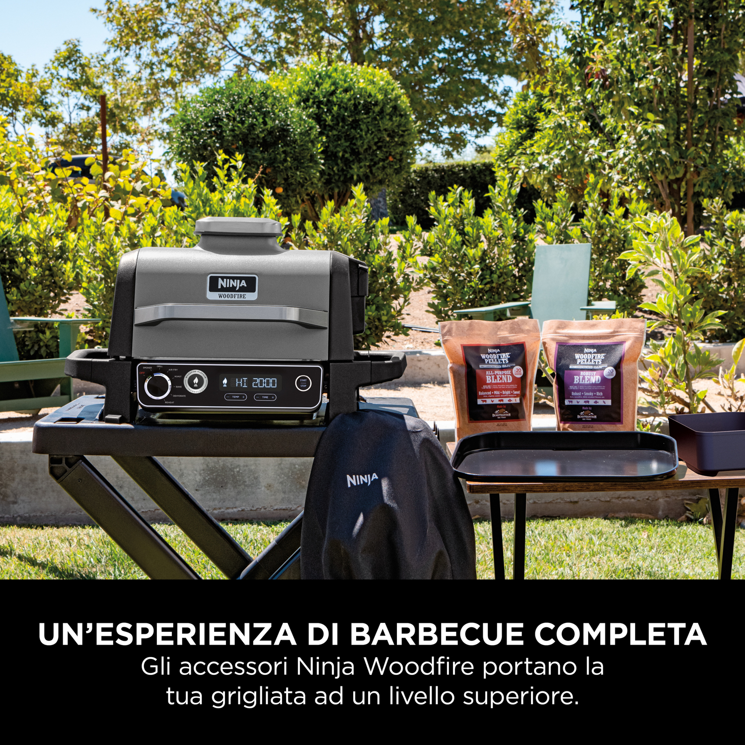 Una griglia Ninja Woodfire su un tavolo in giardino. Due sacchetti di condimento sono a destra della griglia.