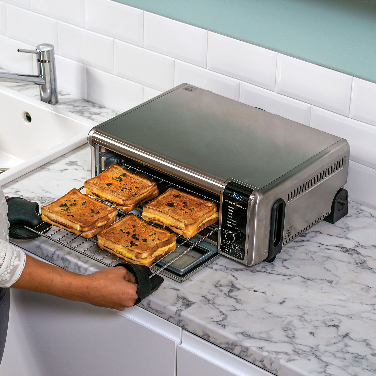 Forno tostapane con panini tostati. Una persona li estrae con un guanto.