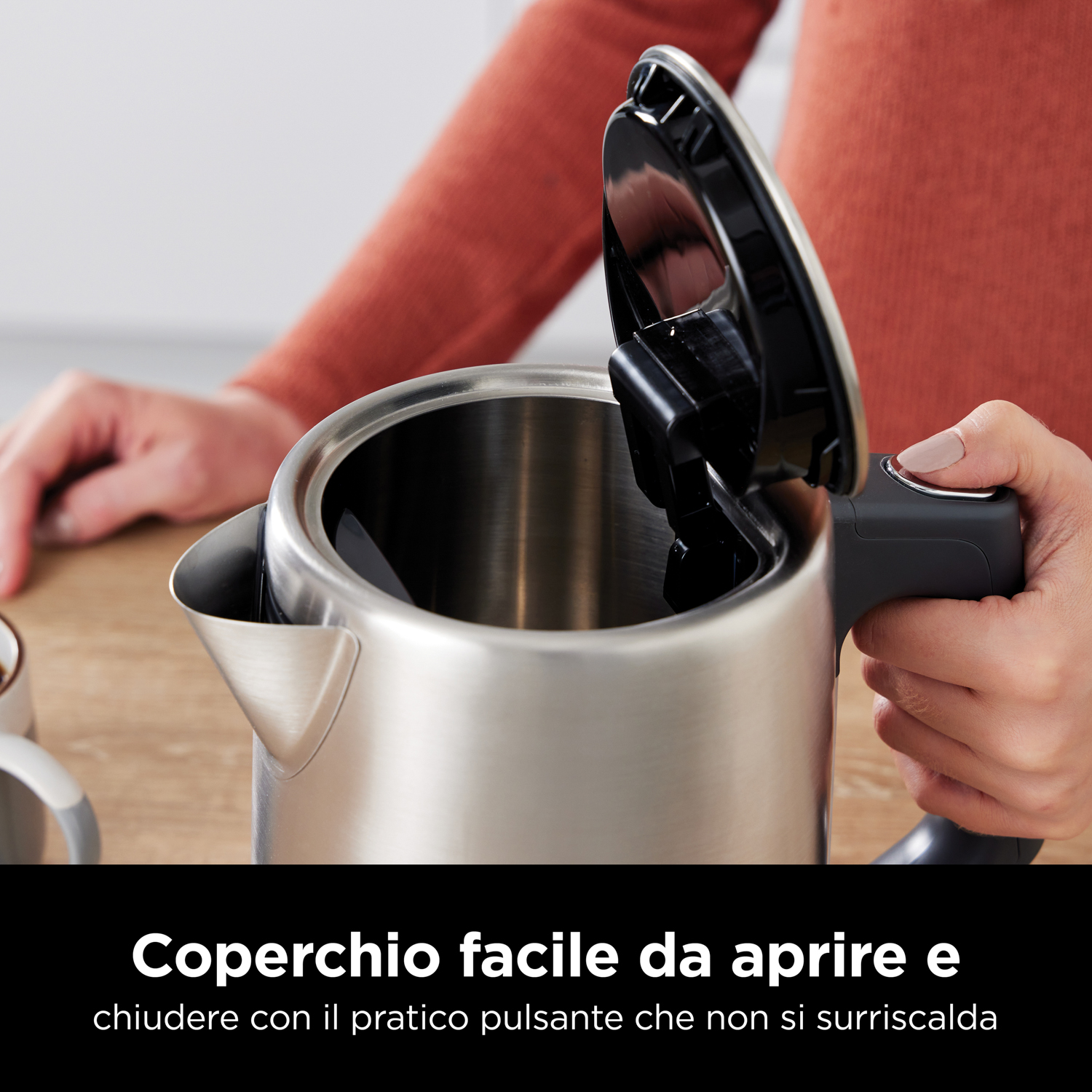 Persona che apre il bollitore con testo: Coperchio facile da aprire. Bollitore in acciaio inox, manico nero.