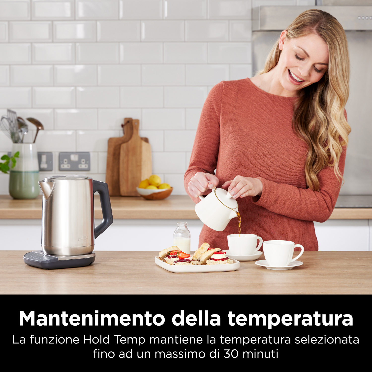 Donna che versa tè da una teiera bianca in una tazza, con un bollitore vicino.