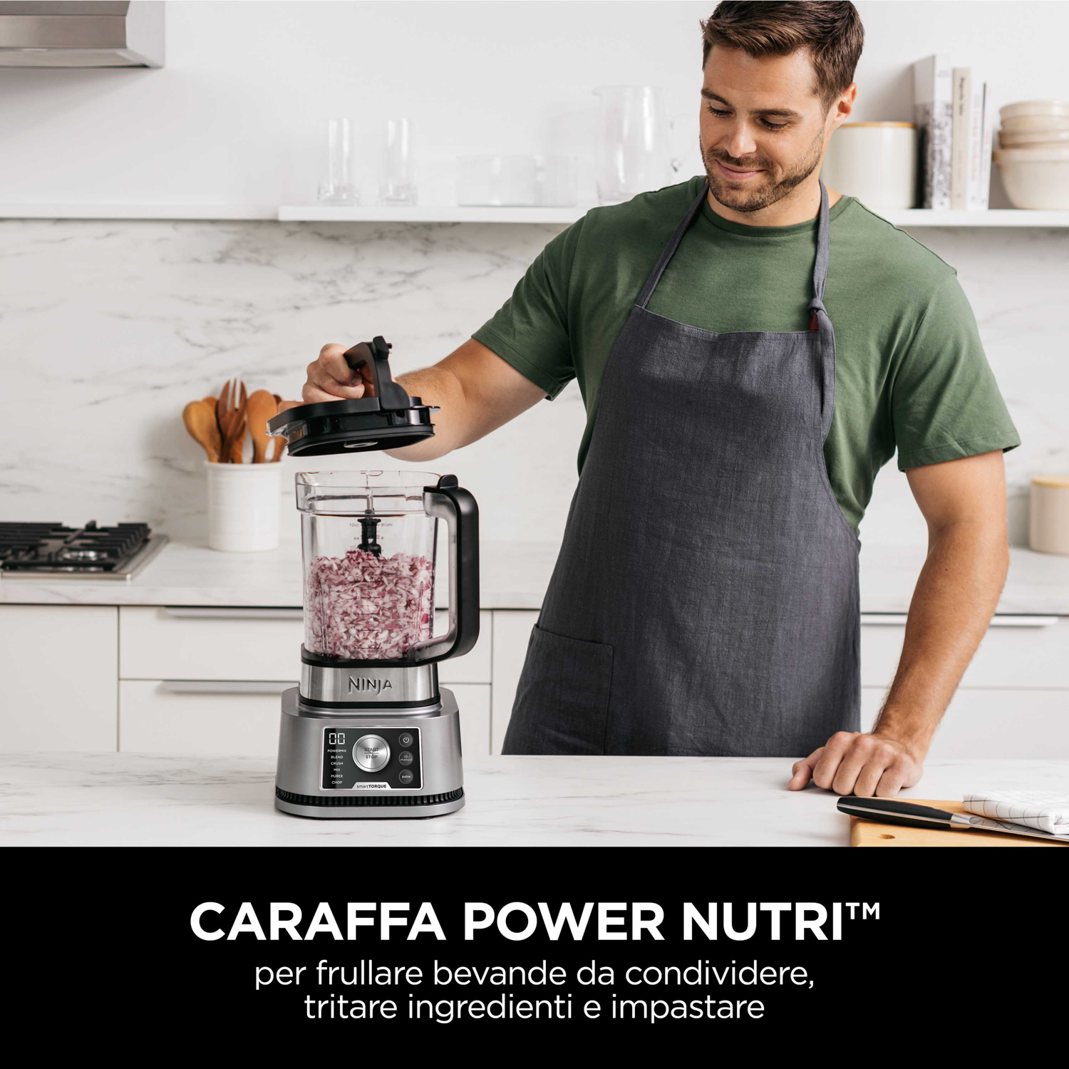 Uomo che usa un frullatore Ninja. Frullatore con ingredienti, uomo con grembiule, cucina bianca.