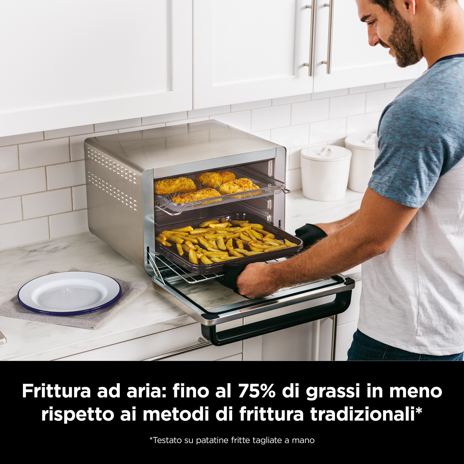 Persona che tira fuori il cibo da una friggitrice ad aria argentata. Patatine fritte e pollo all'interno, su un bancone bianco.