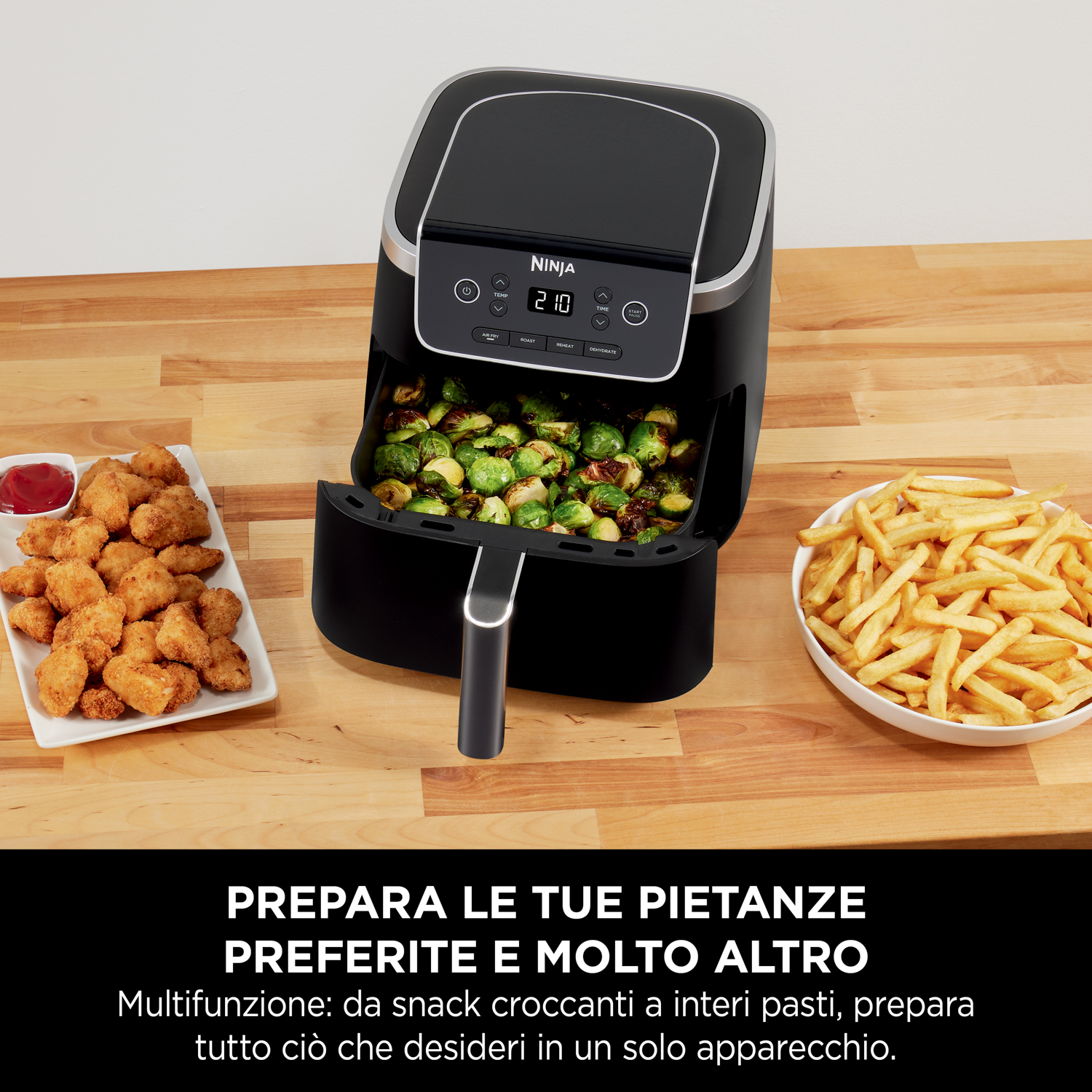 Una friggitrice ad aria nera con un vassoio di cavoletti di Bruxelles, un piatto di pepite di pollo e una ciotola di patatine.