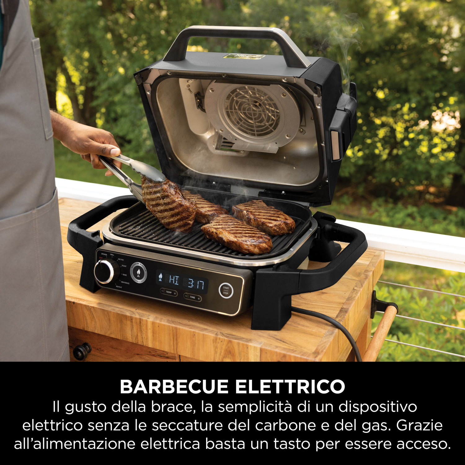 Uomo usa le pinze per girare le bistecche su una griglia elettrica. Tavolo di legno e ventola.