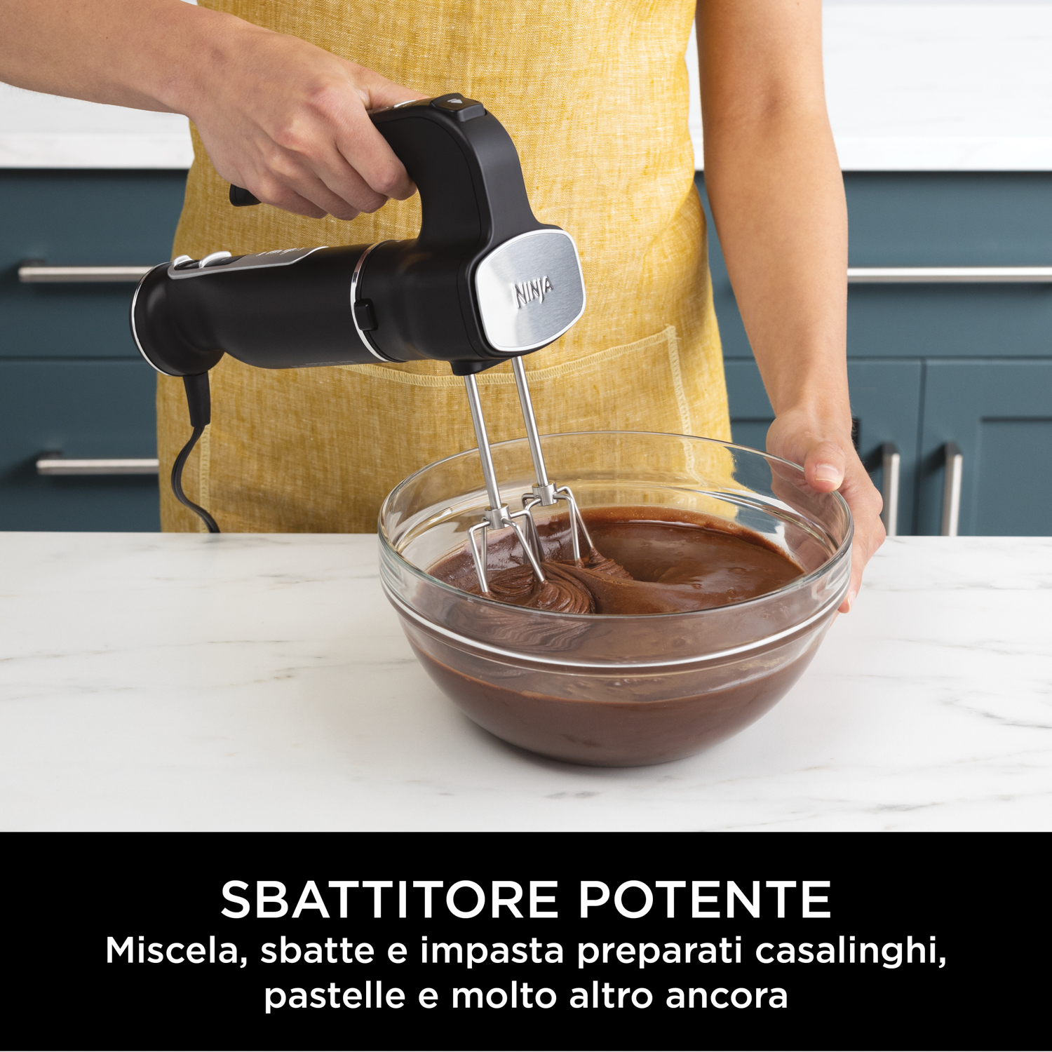 Frullatore a mano che mescola cioccolato in una ciotola. Persona con grembiule giallo. Lo sfondo è una cucina.