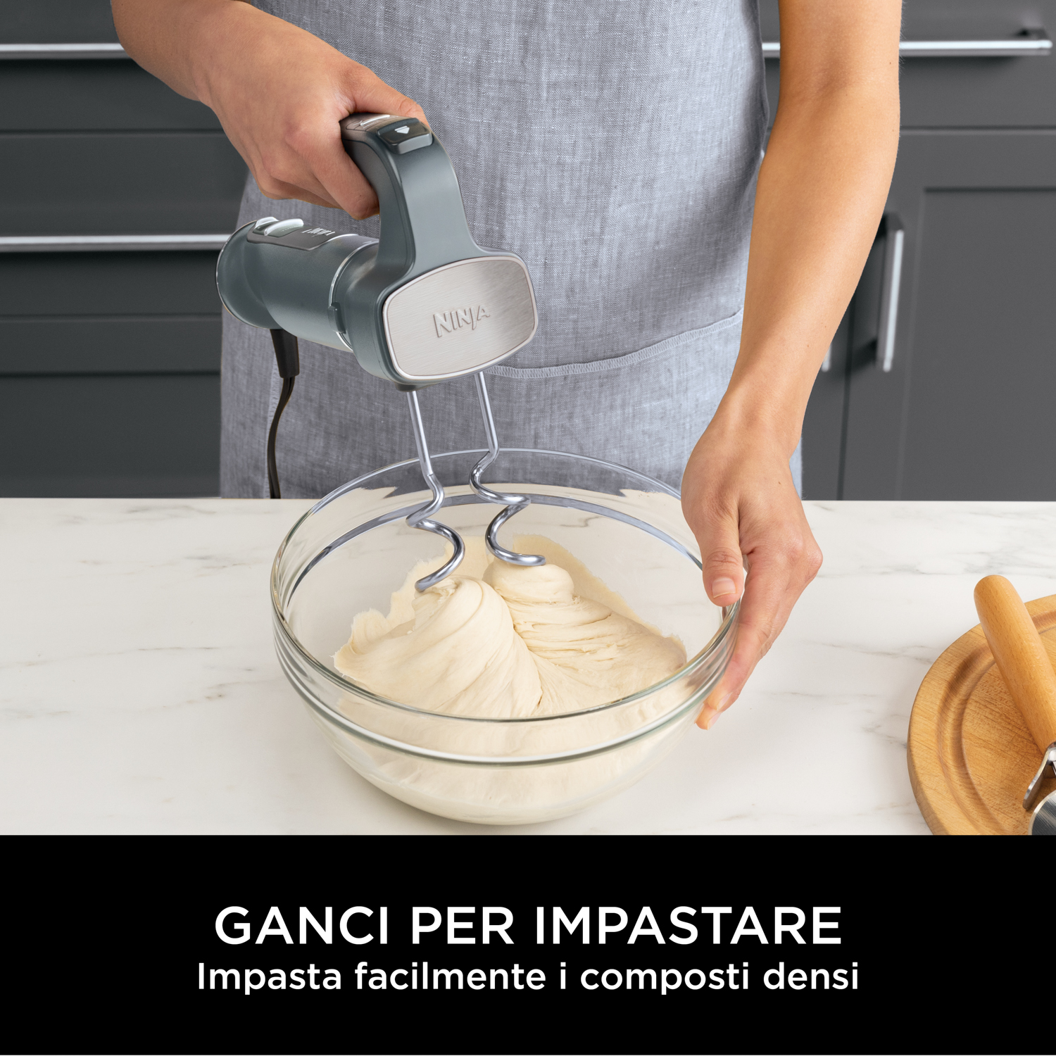 Una persona mescola l'impasto in una ciotola di vetro con un frullatore a mano. L'impasto è nella ciotola. C'è un matterello.