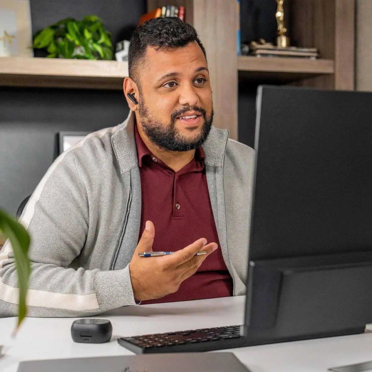 Mann in grauer Jacke und weinrotem Hemd, benutzt einen Stift. Er trägt Ohrhörer und schaut auf einen Computerbildschirm, mit Tastatur.
