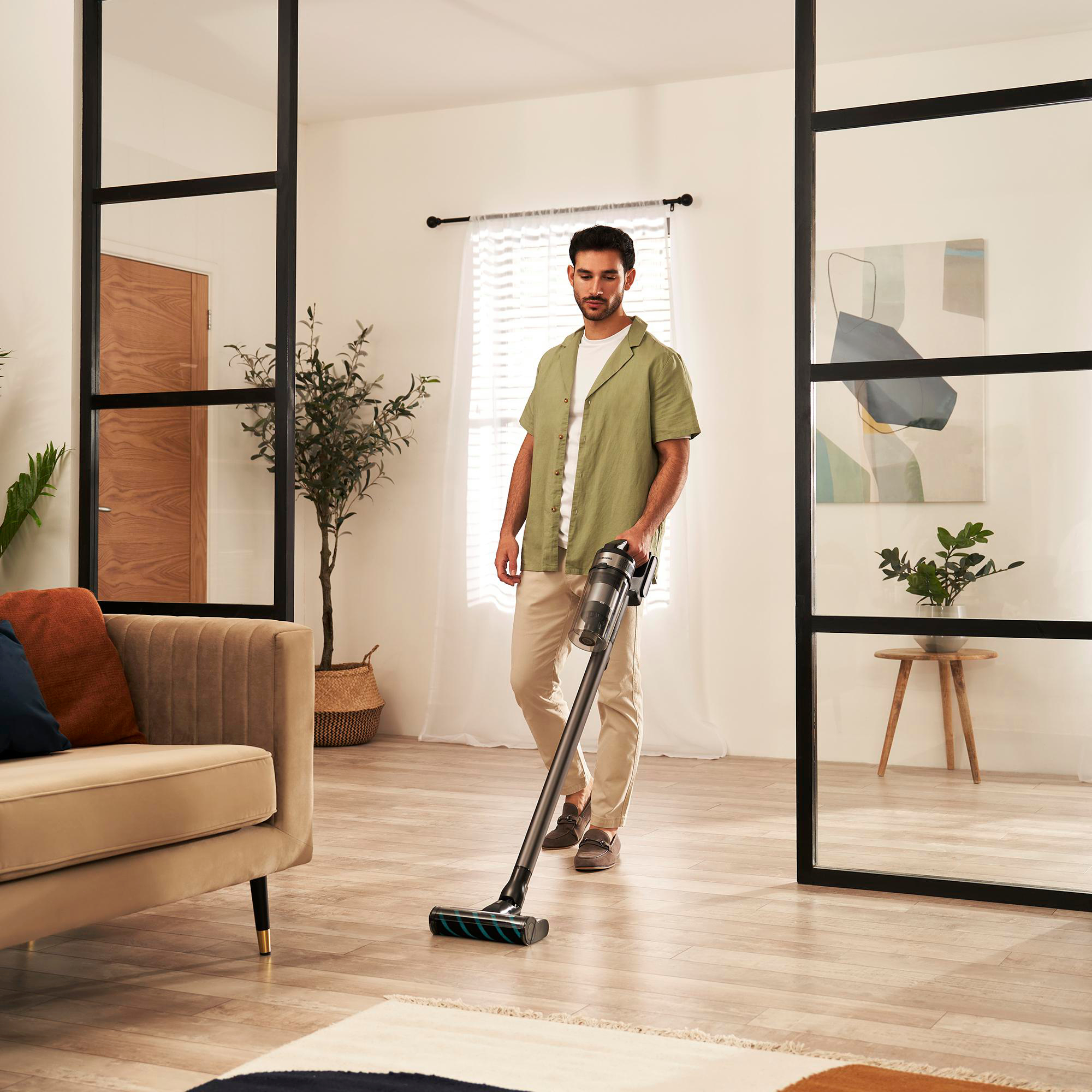 Ein Mann, der den Boden saugt. Er befindet sich in einem Raum mit Glastüren und einem Sofa.
