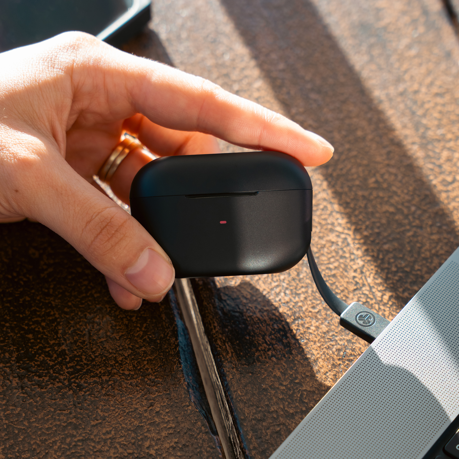 Hand holding black charging case connected to a laptop via cable.