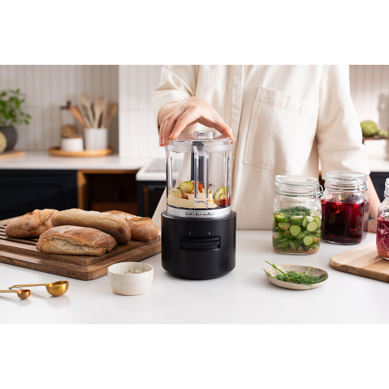 Una persona utilizza un piccolo robot da cucina KitchenAid nero. Pane e barattoli sul tavolo.