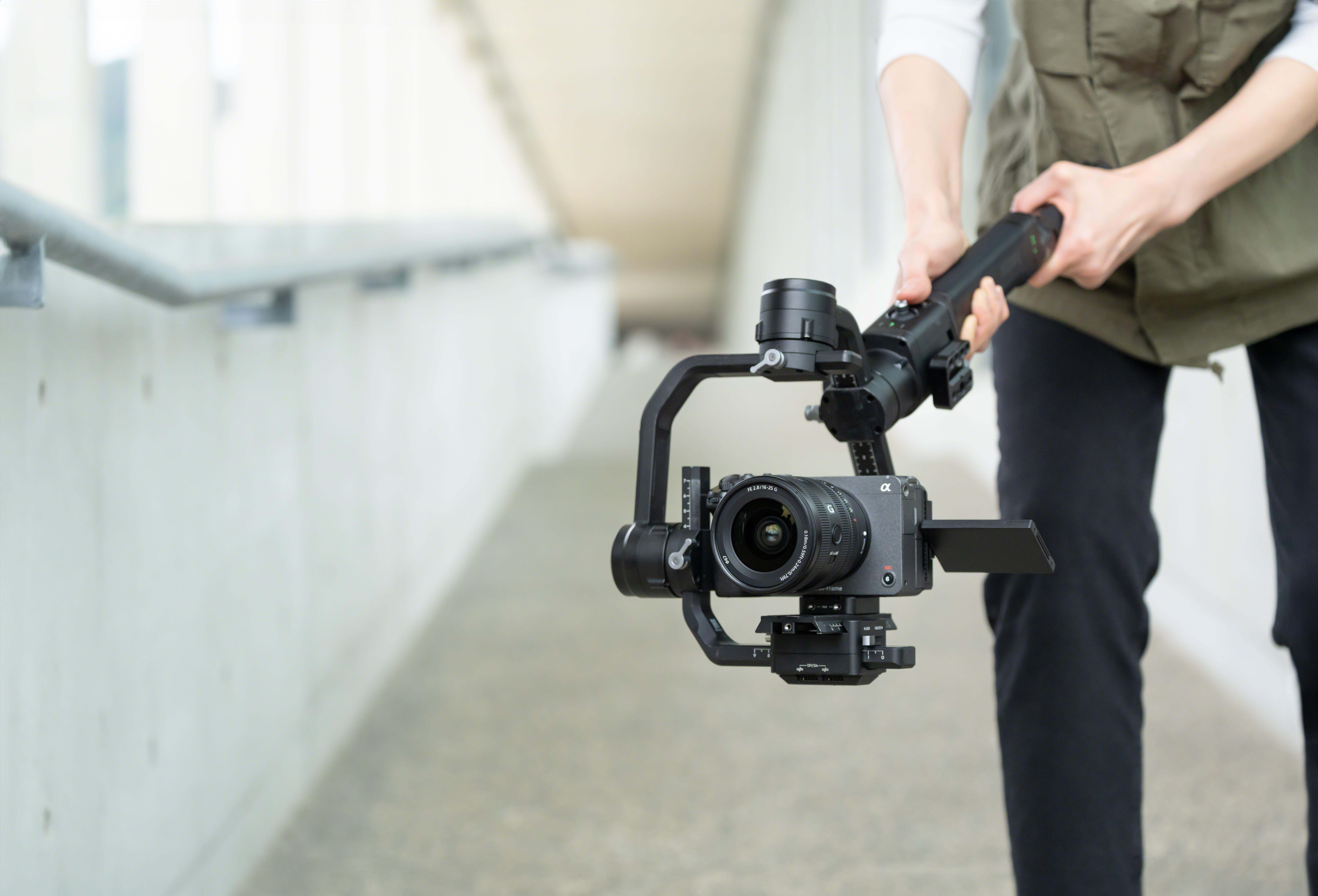 Eine Person hält eine Kamera auf einem Gimbal. Die Person befindet sich in einem modernen, offenen Raum.