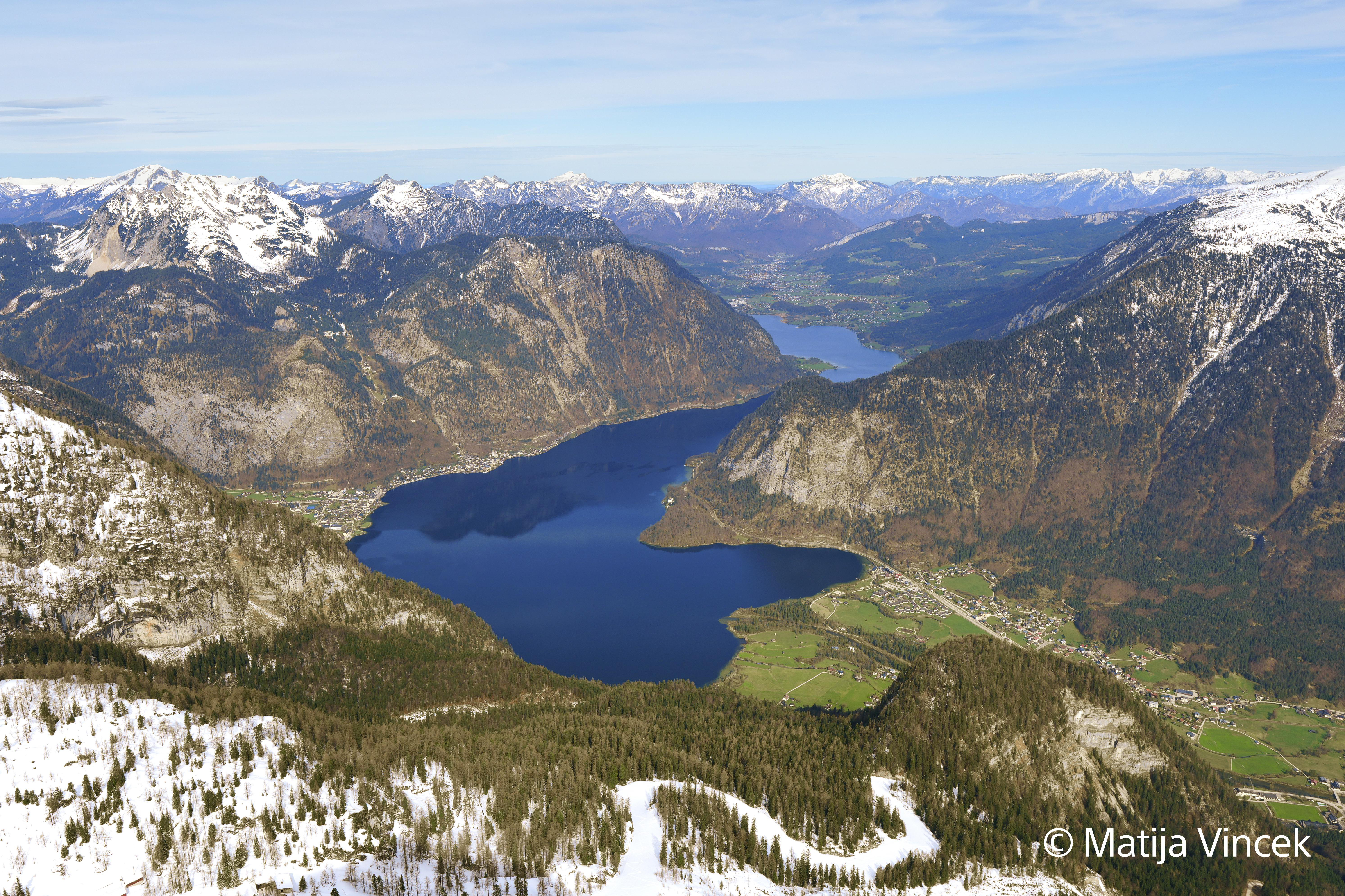 Luftaufnahme eines Sees, umgeben von Bergen mit schneebedeckten Gipfeln.