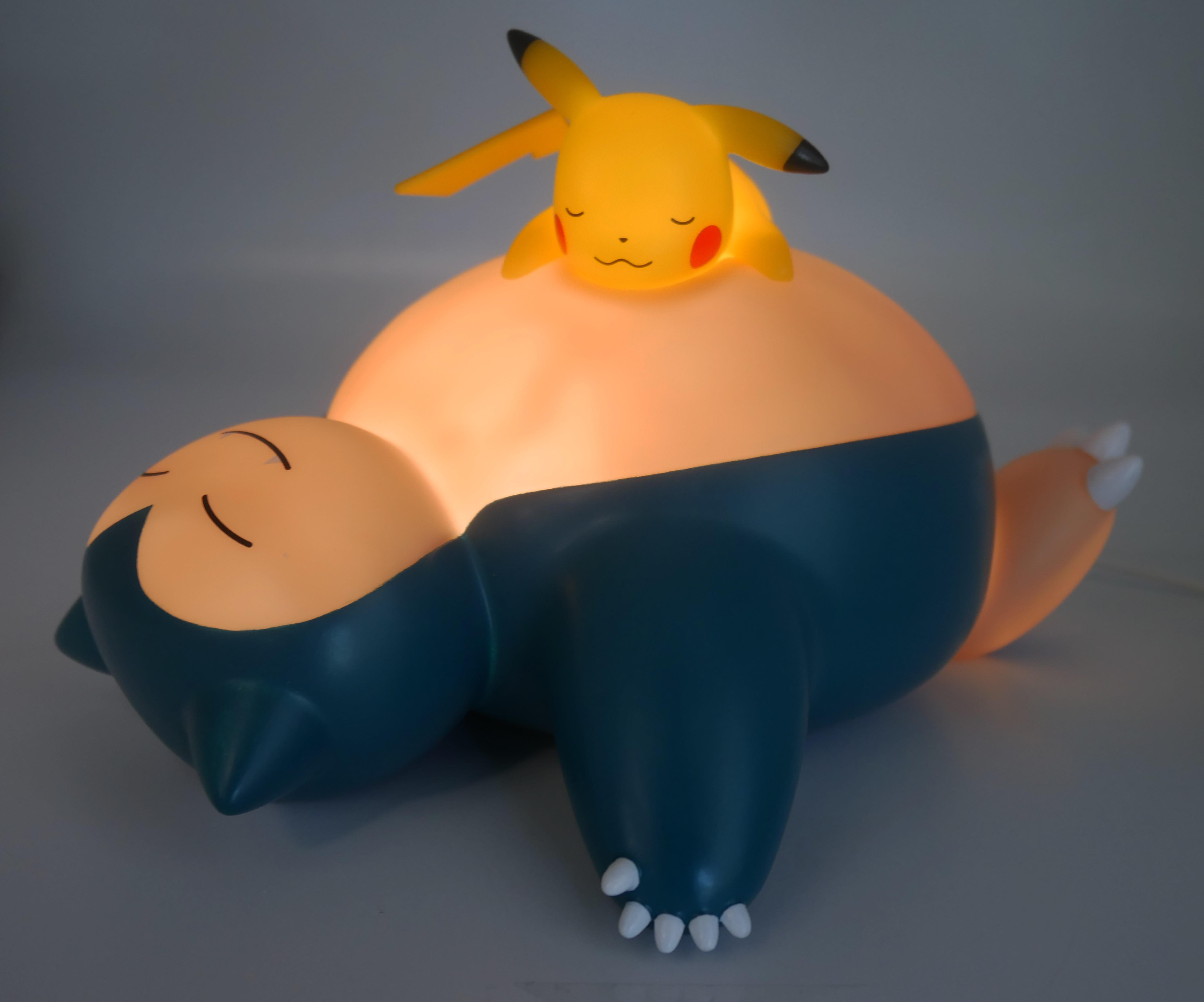 Eine Snorlax-Lampe mit Pikachu oben drauf, beleuchtet.