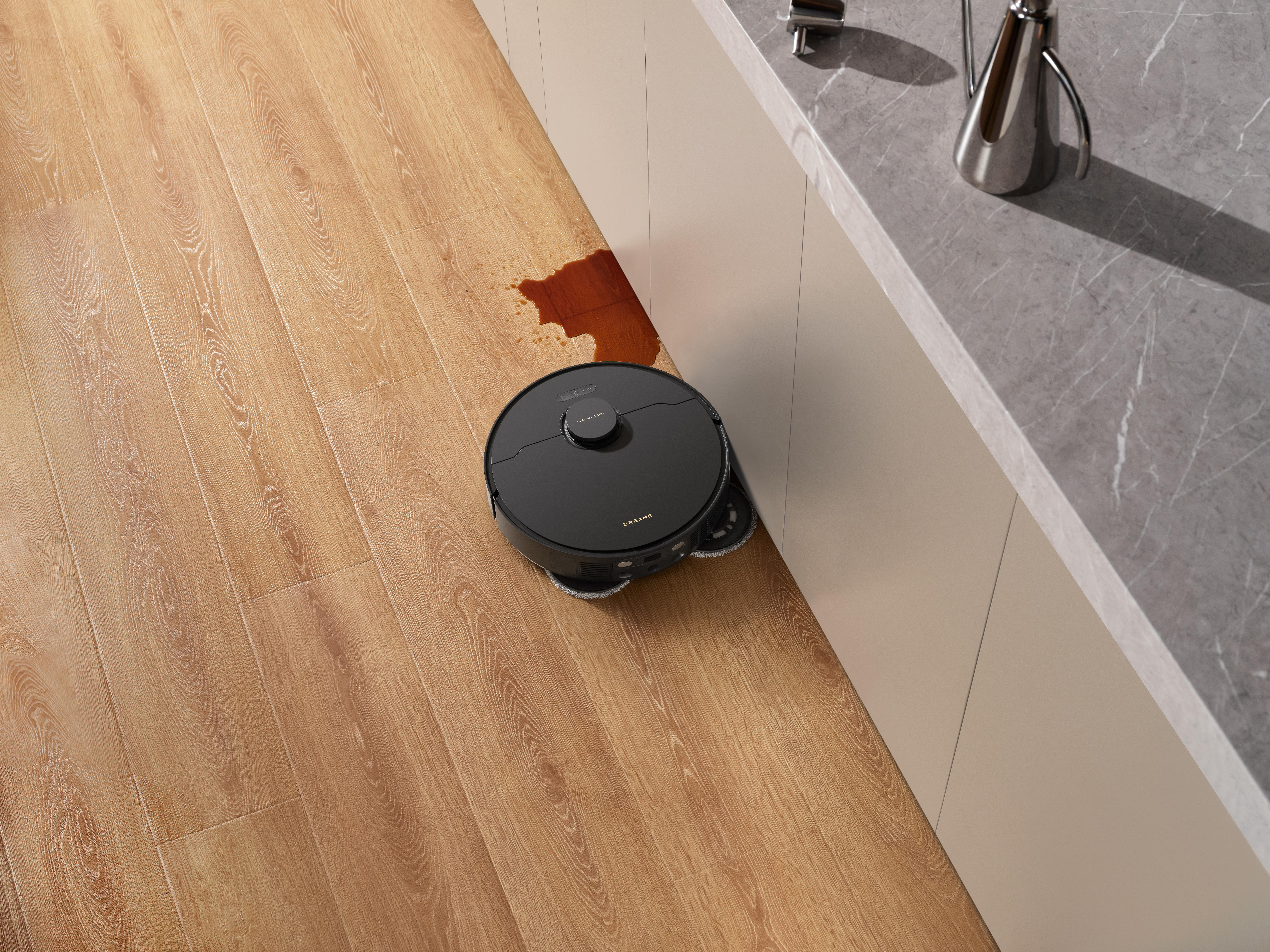 Ein schwarzer Roboter-Staubsauger reinigt einen Holzboden. Ein Fleck ist vorhanden.