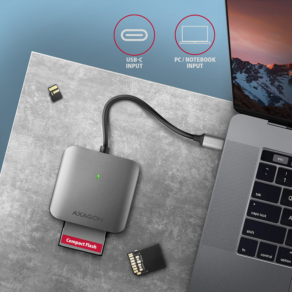 Egy ezüst Axagon kártyaolvasó egy behelyezett Compact Flash kártyával és egy laptop. USB és PC bemenetek láthatók.