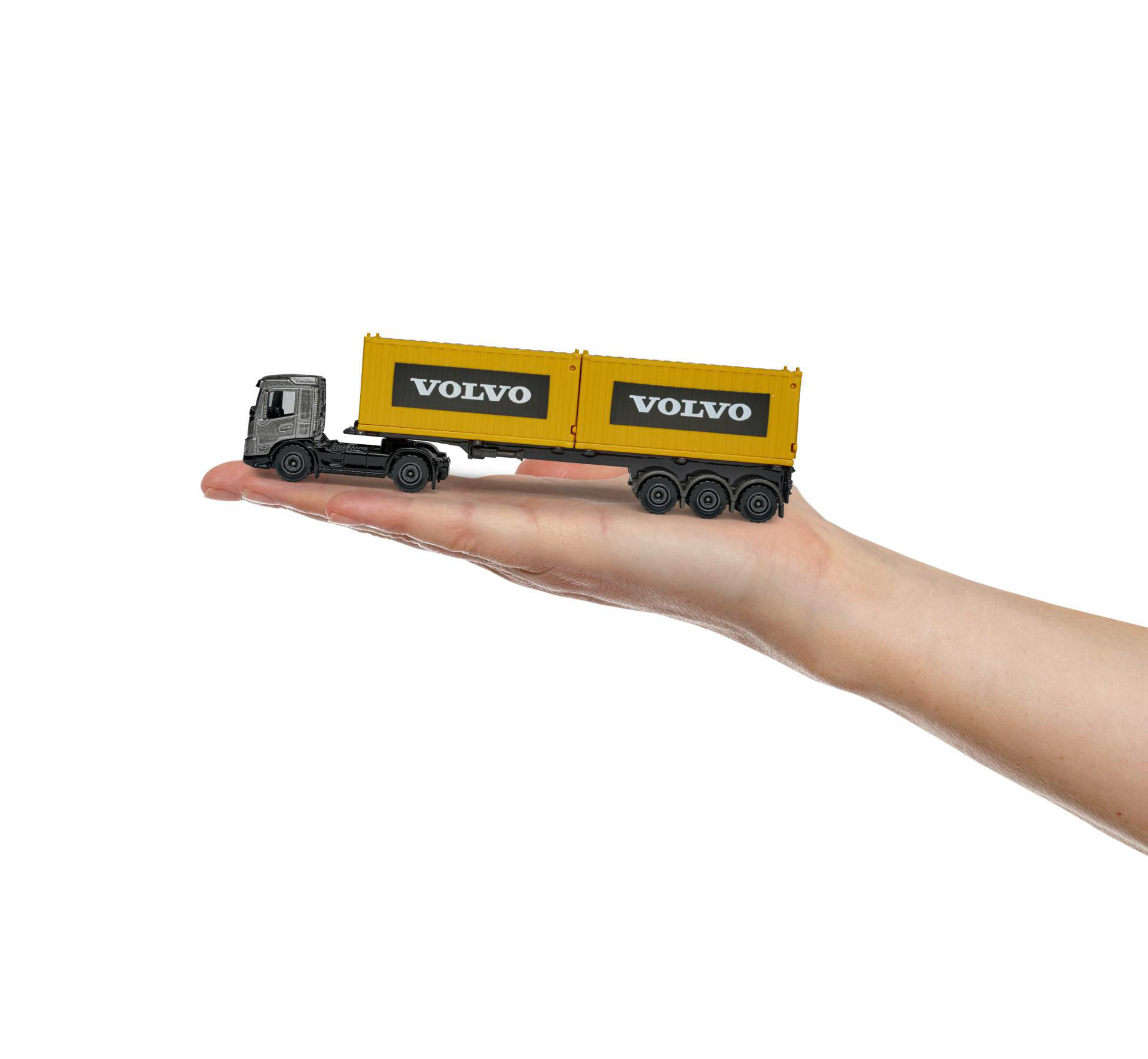 Spielzeug-LKW auf einer Hand. Gelber Anhänger mit 'VOLVO', graues Fahrerhaus. Weißer Hintergrund.