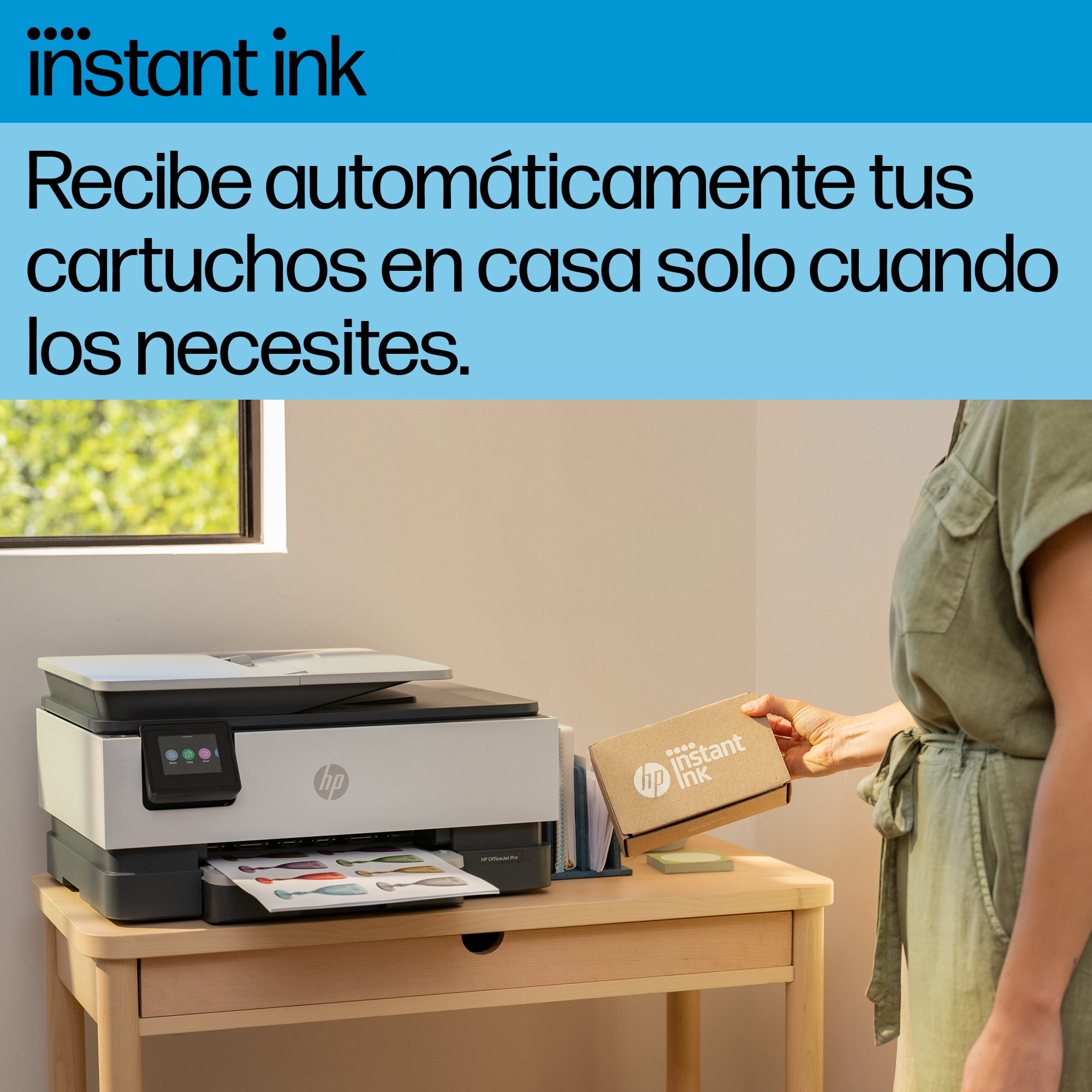 Mujer sosteniendo una caja con el logo 'Instant Ink', cerca de una impresora en una mesa, en casa.