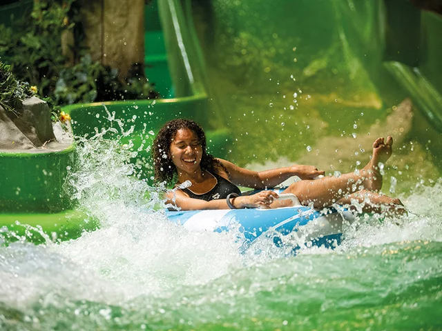 Une femme sur une bouée bleue éclabousse dans un parc aquatique. Elle sourit et l'eau l'éclabousse.