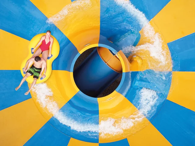 Vue aérienne d'un toboggan aquatique. Deux personnes sur un radeau jaune descendent.