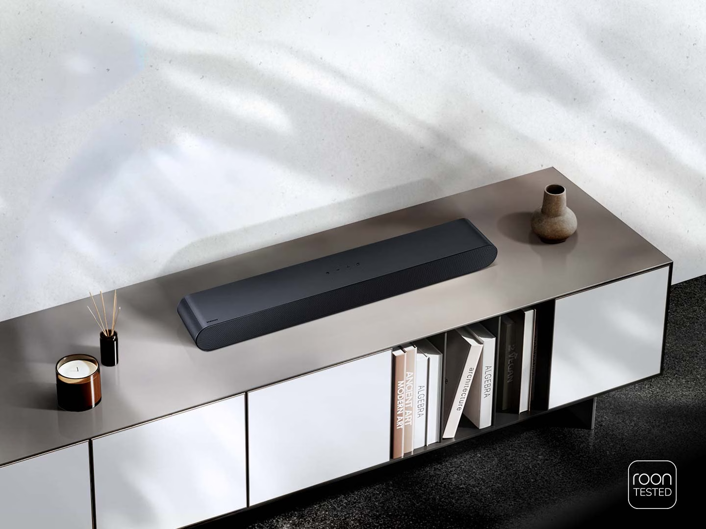 Une barre de son sombre et moderne sur un meuble, avec des livres, une bougie et un vase.