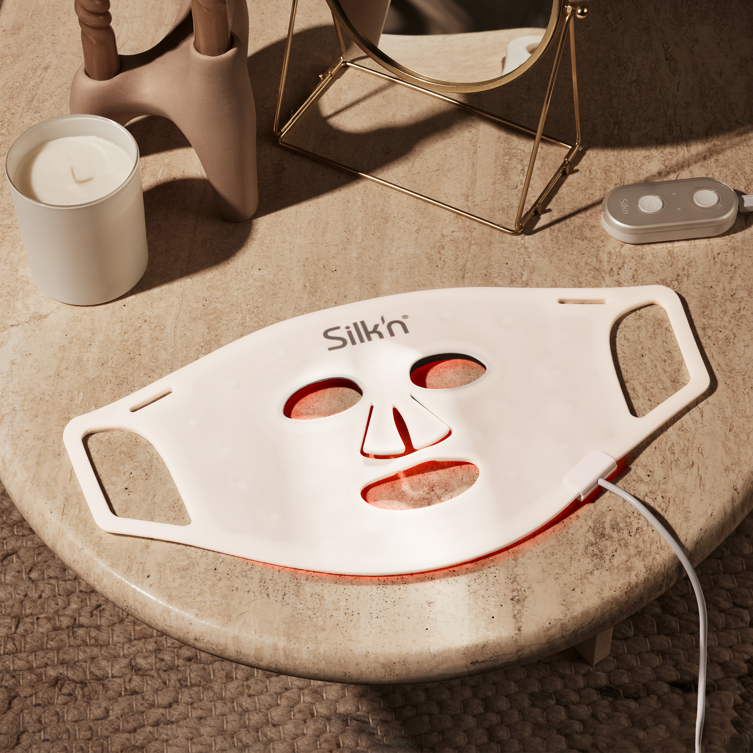 Silk'n LED gezichtsmasker op een tafel. Rood licht dat uit het masker komt. Verschillende items rondom het masker.