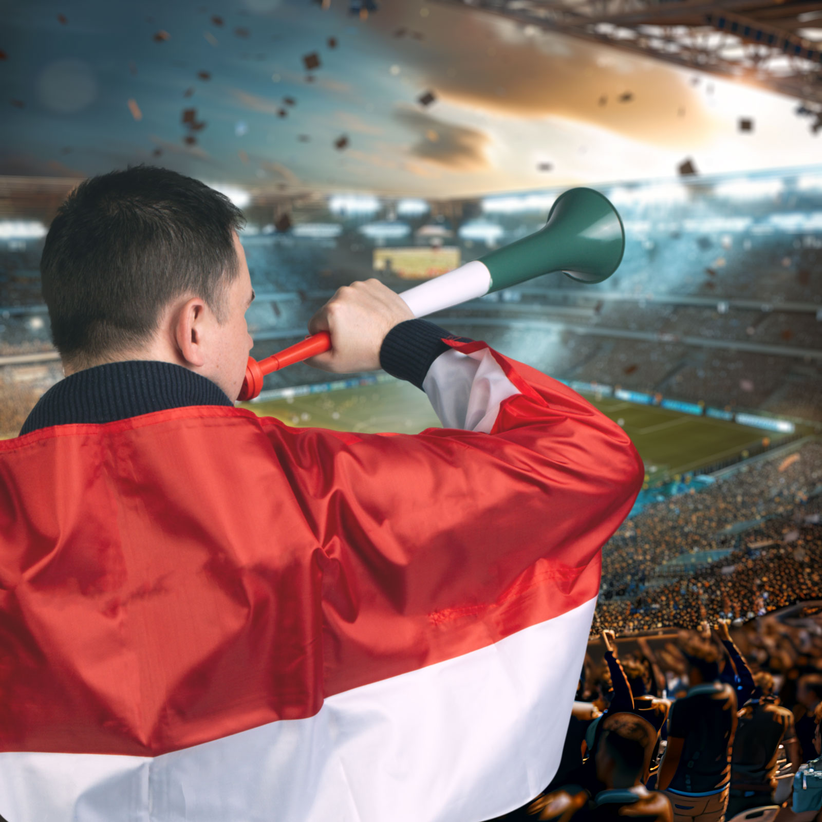 Egy férfi kürttel fúj egy stadionban, nagy tömeggel és egy futballpályával.