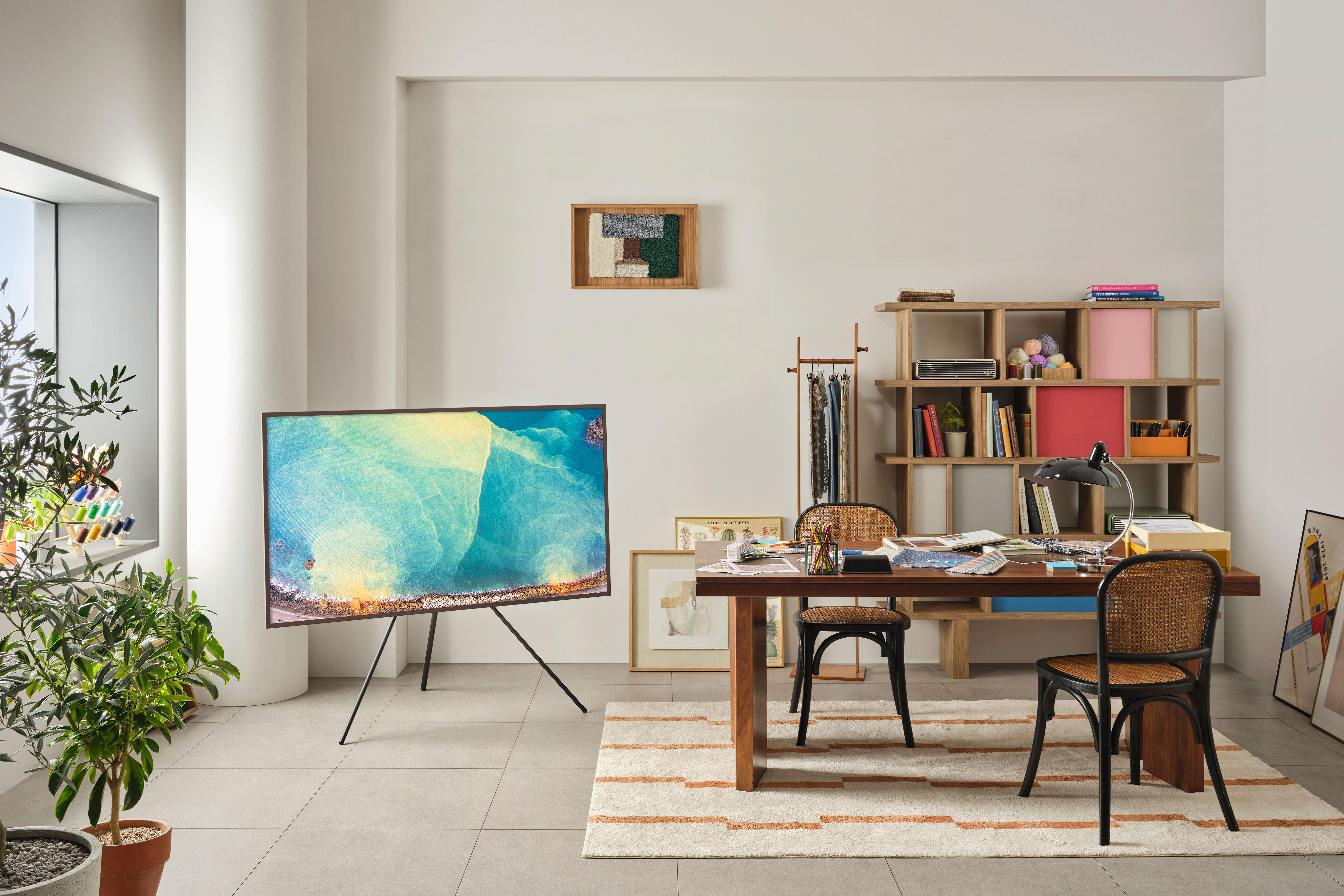 Wohnzimmer mit Fernseher auf einem Ständer, Schreibtisch und Regal.