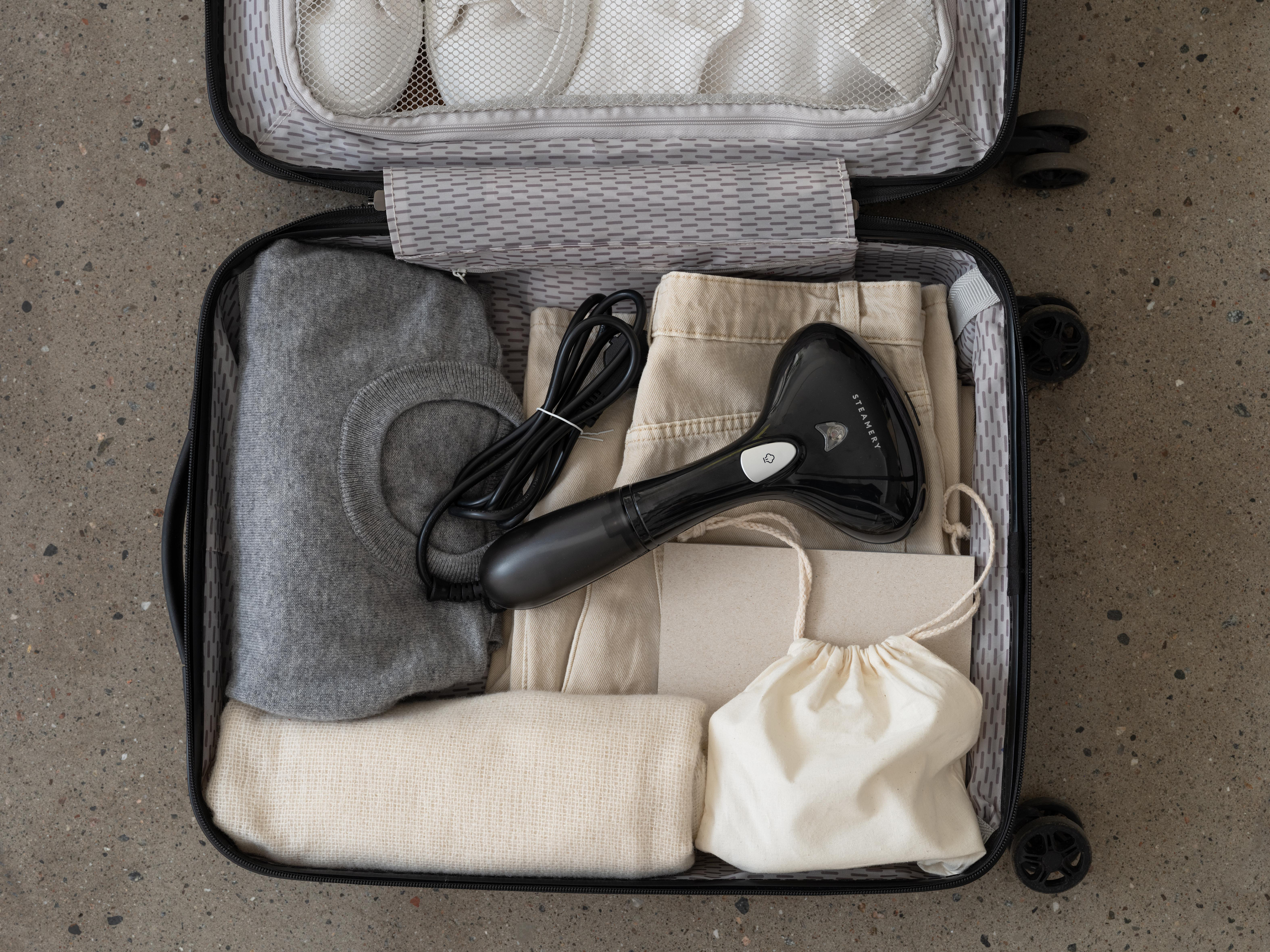 Ein offener Koffer, gepackt mit Kleidung, einem Steamer und anderen Reiseutensilien.