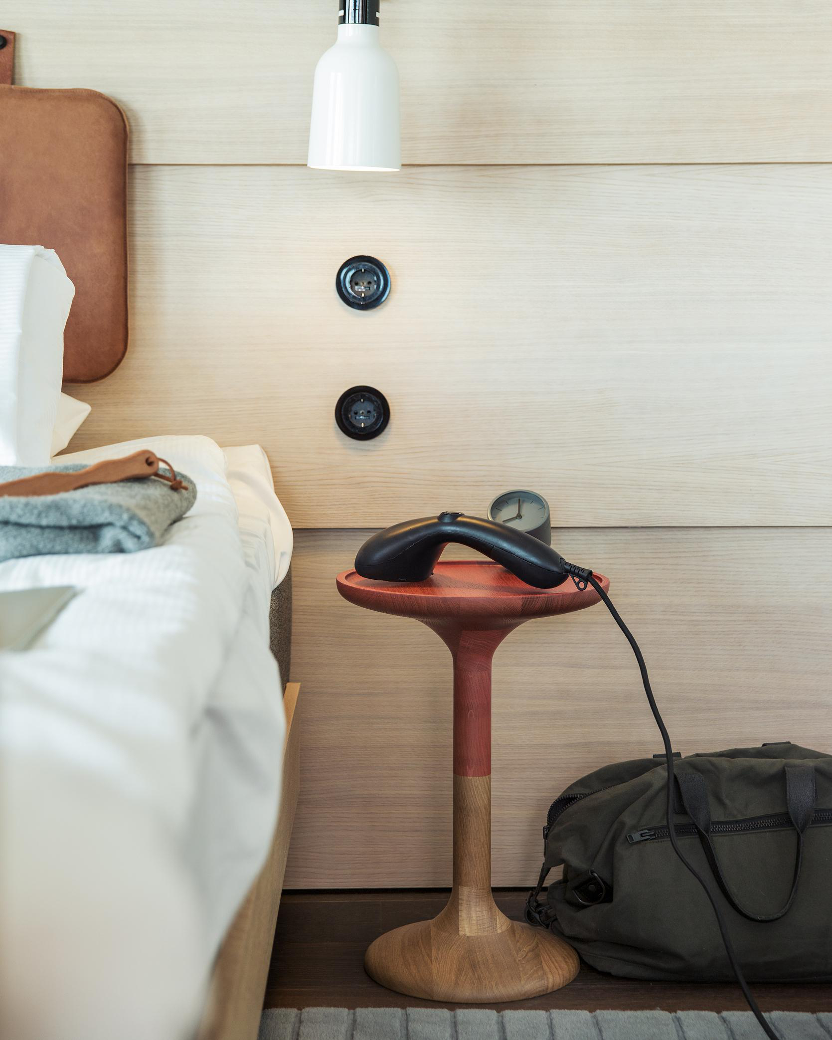 Schlafzimmer-Szene mit einem Dampfgarer auf einem Beistelltisch. Bett links. Wand helles Holz.