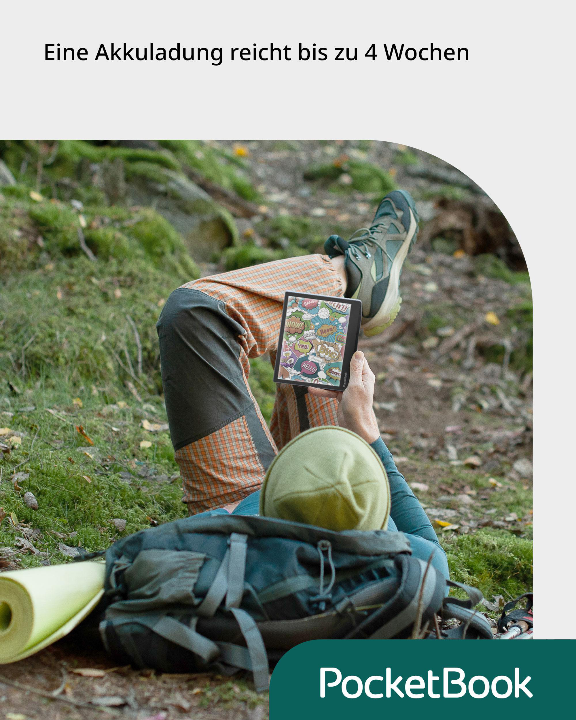 Person liegt im Gras und liest ein PocketBook, mit Rucksack und Wald.