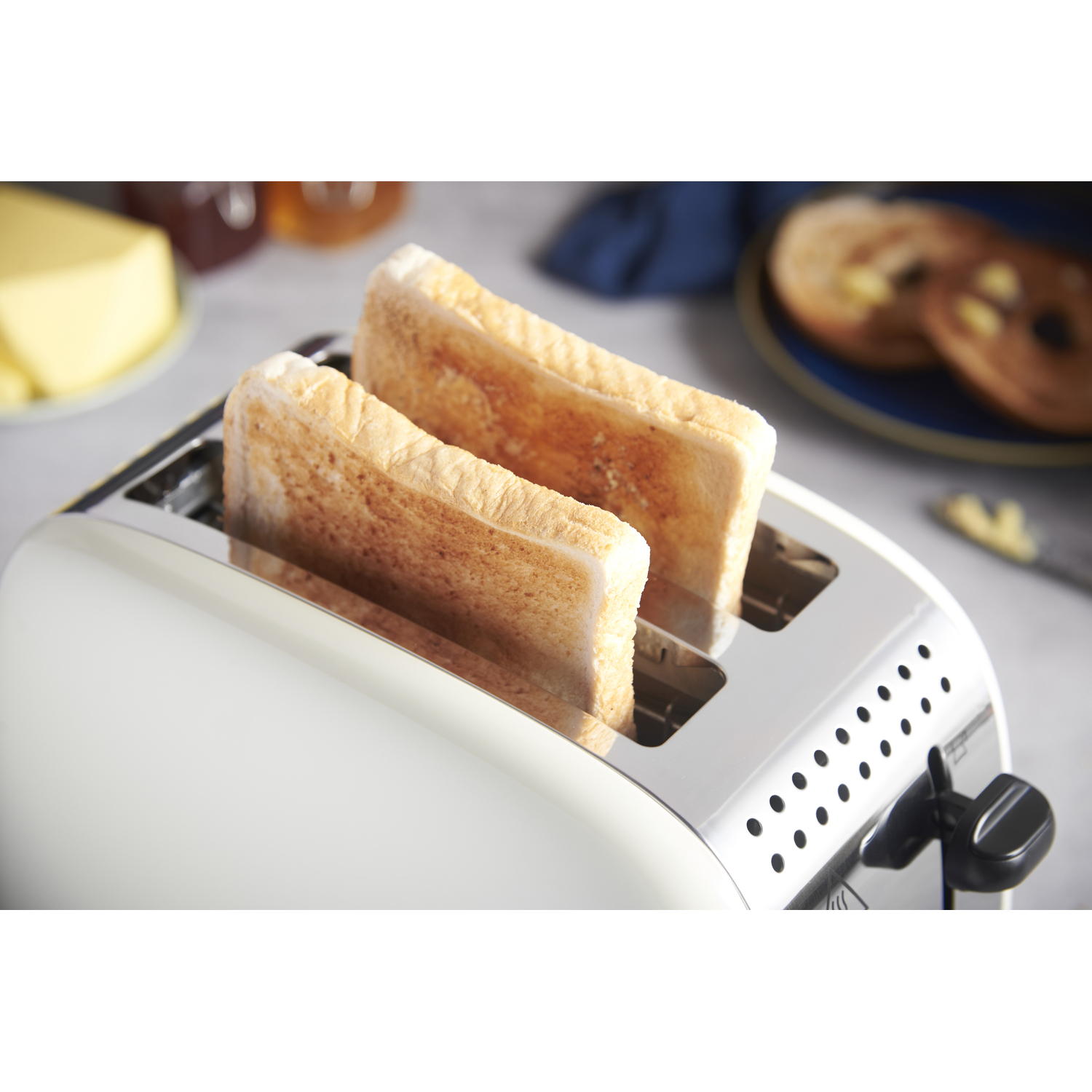 Toaster with two slices of toast. Butter and jam in the background.