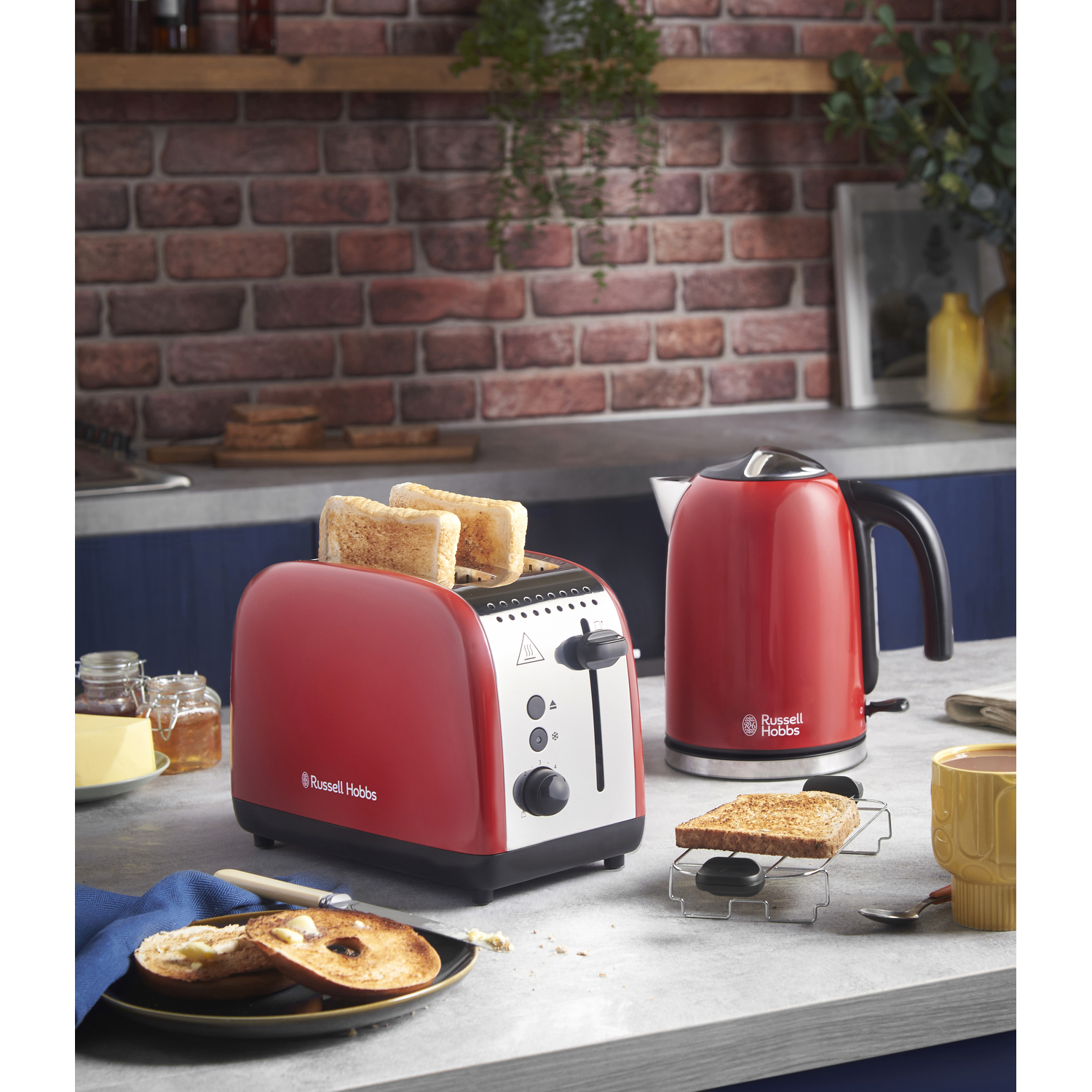 Red toaster with toast and a red kettle on a counter, brick wall background.