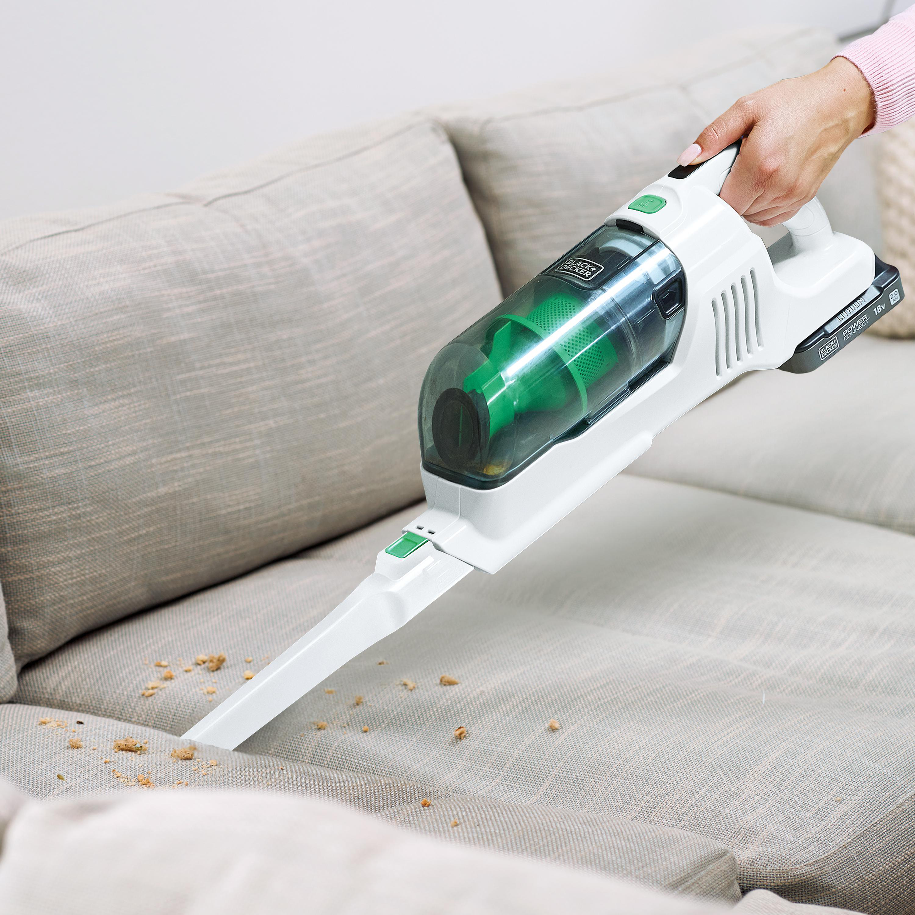 Handstaubsauger, der Krümel von einem grauen Sofa reinigt.