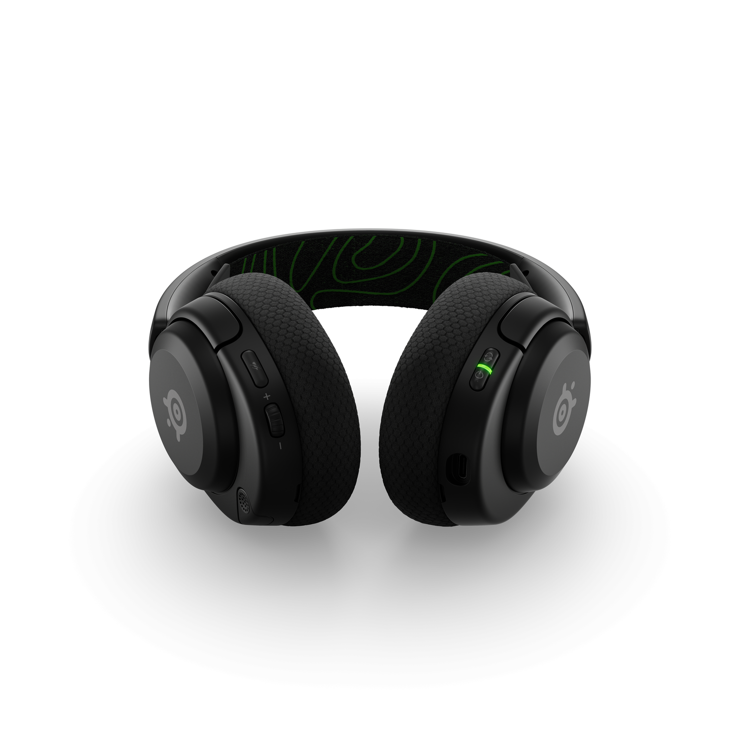 Black SteelSeries headphones with green design accents, lying on a white surface.