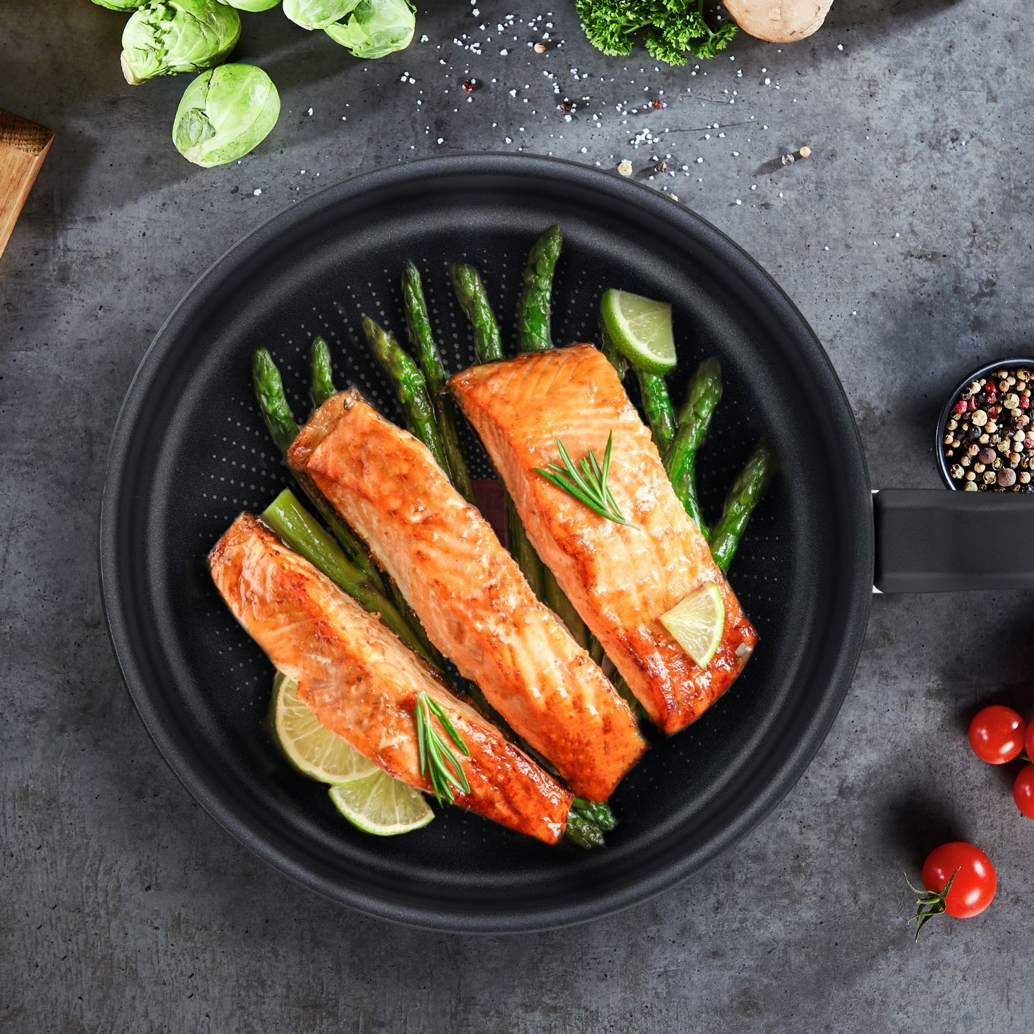 Salmon fillets with asparagus and lime on a black pan. Vegetables and spices in the background.