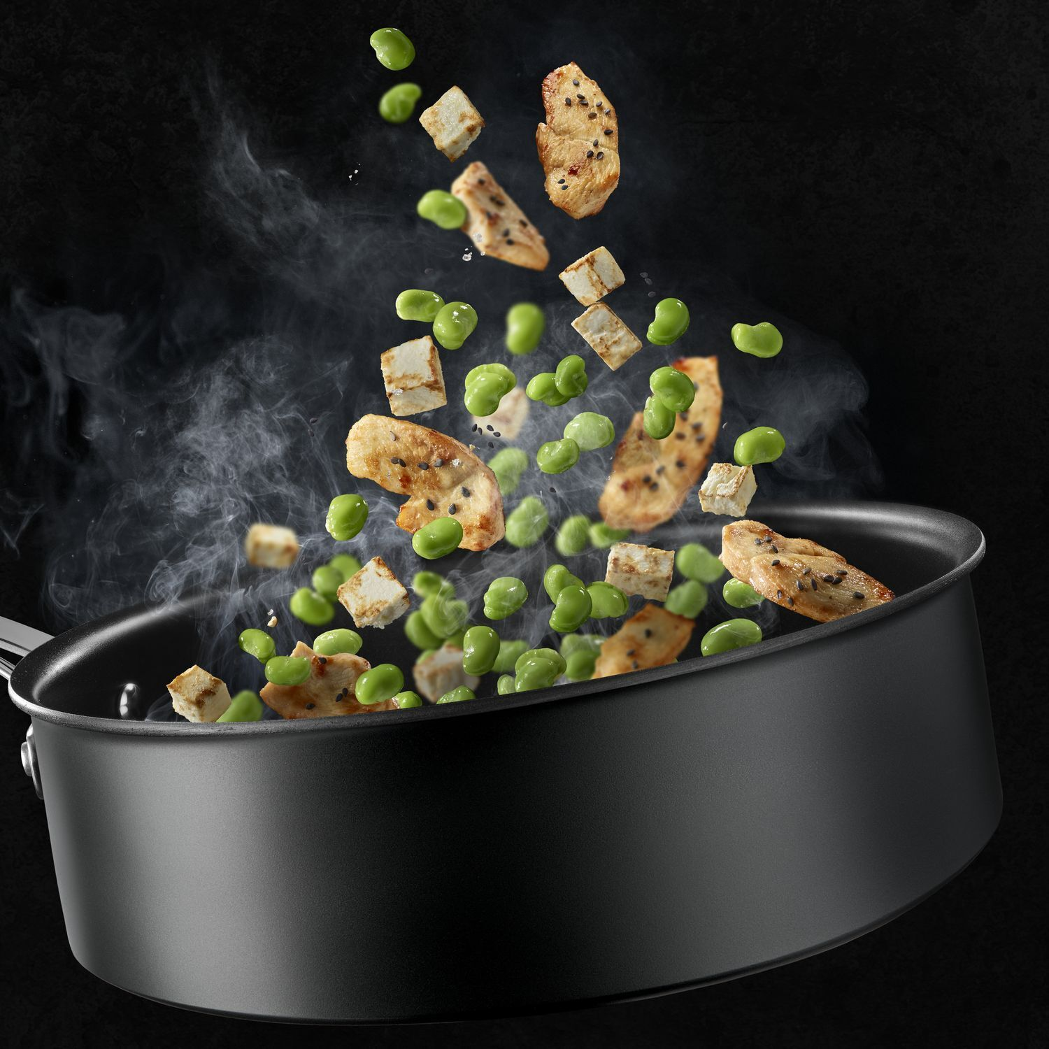 Food and steam are rising out of a black pan. There are tofu and peas. Black background.