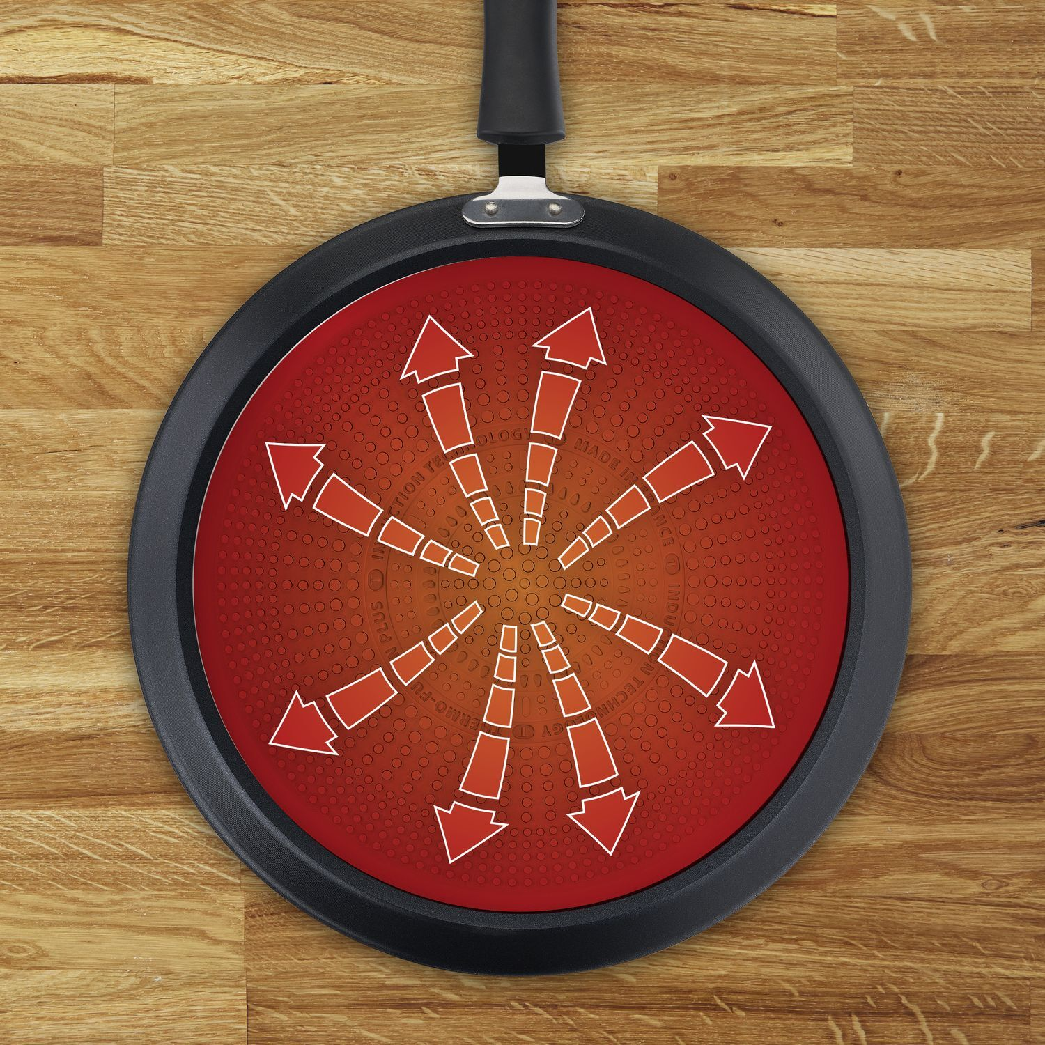 A black frying pan with a red interior and white arrows on a wooden surface.