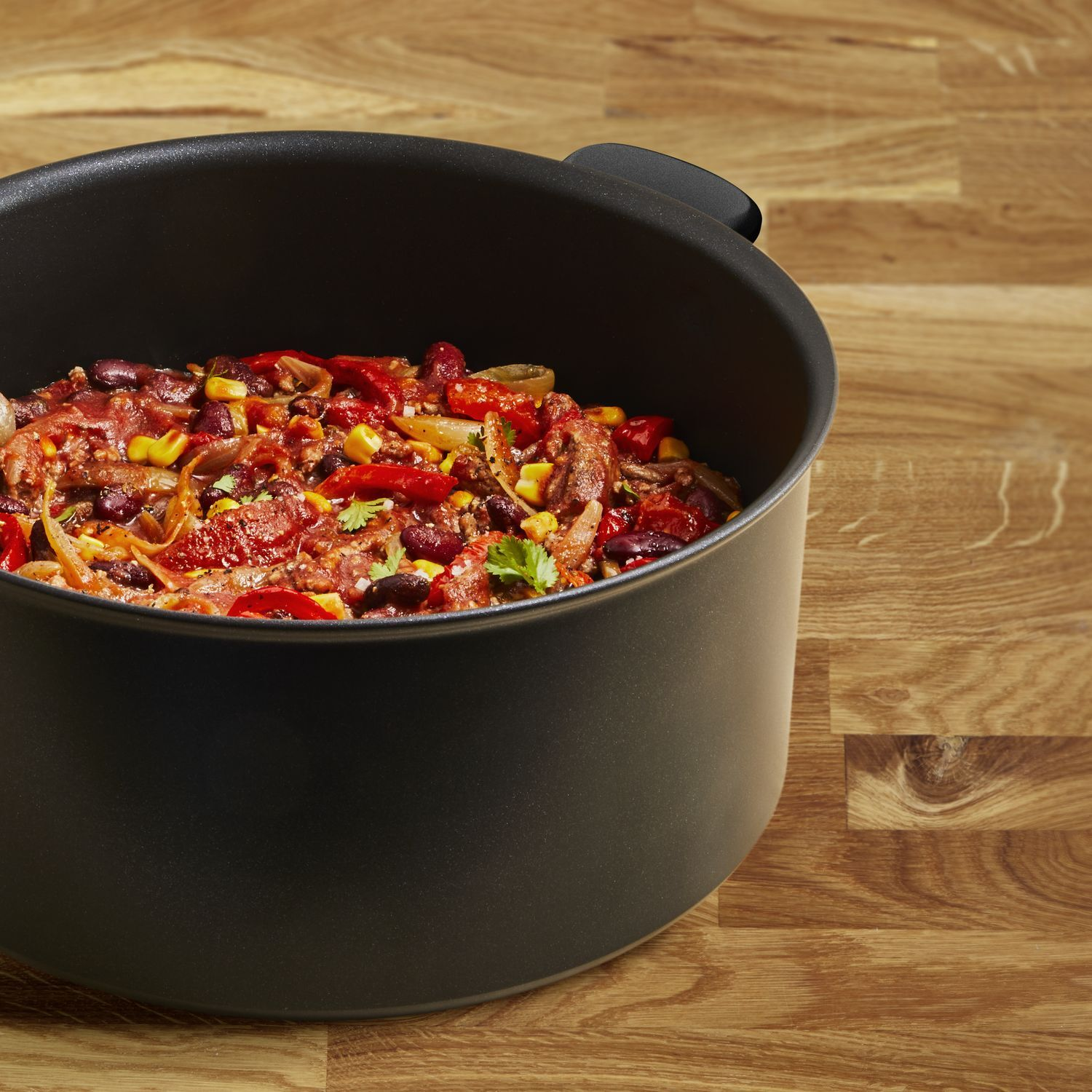A black pot filled with chili. The chili contains beans, corn, tomatoes, and cilantro.