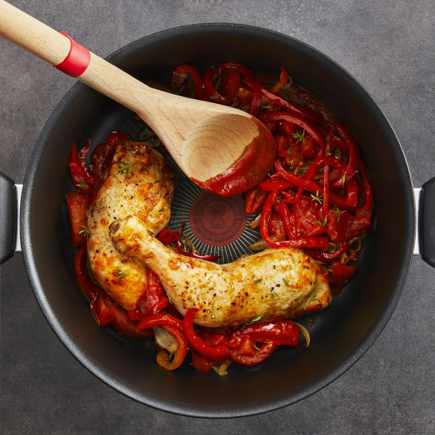 Chicken and red peppers cooking in a pan with a wooden spoon. Overhead shot.