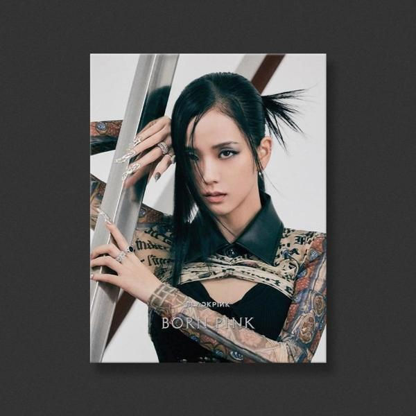 Frau in schwarzem Top und Tattoos, lehnt an einer Metallstange, blickt in die Kamera.