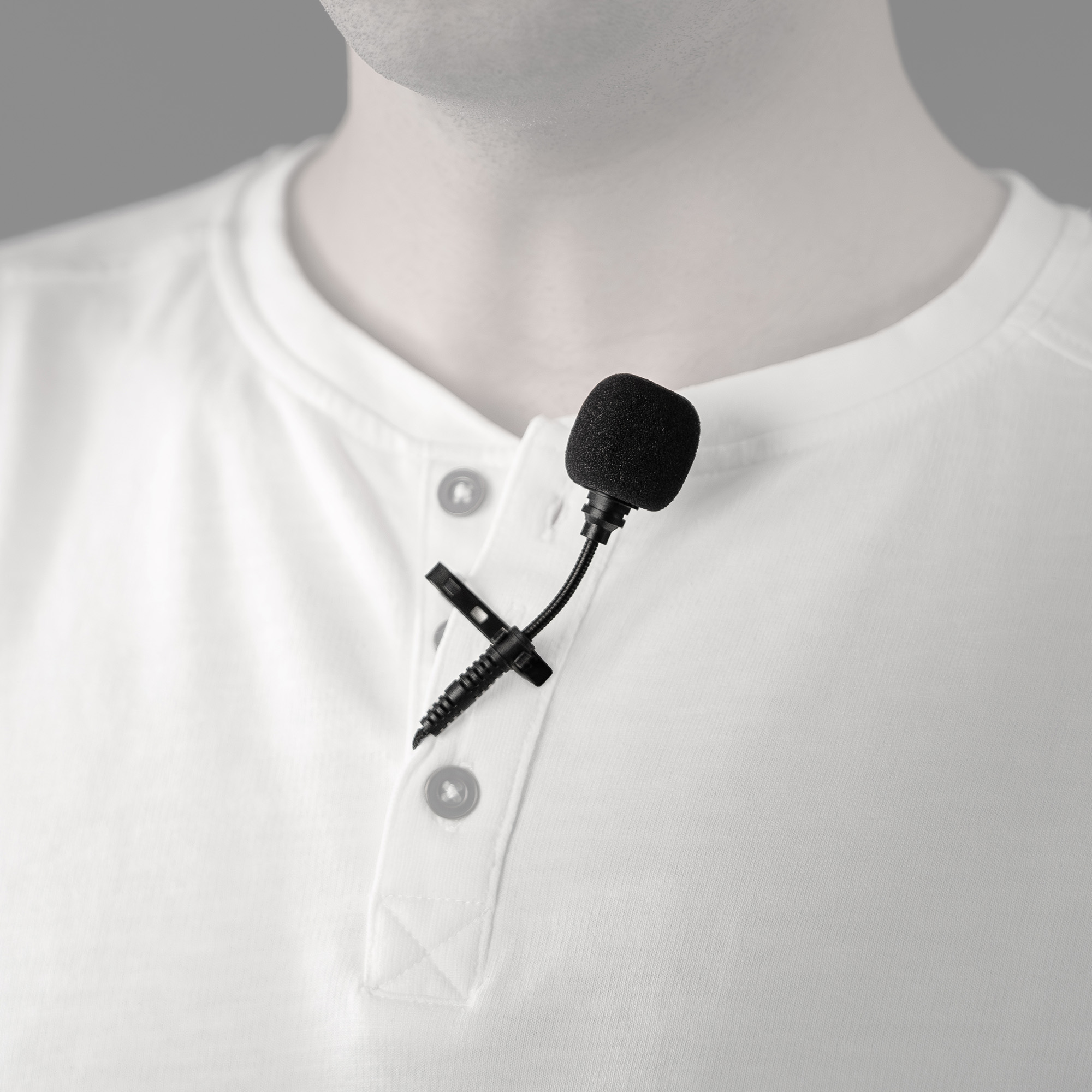 Un hombre con una camisa blanca tiene un pequeño micrófono negro sujeto al cuello.
