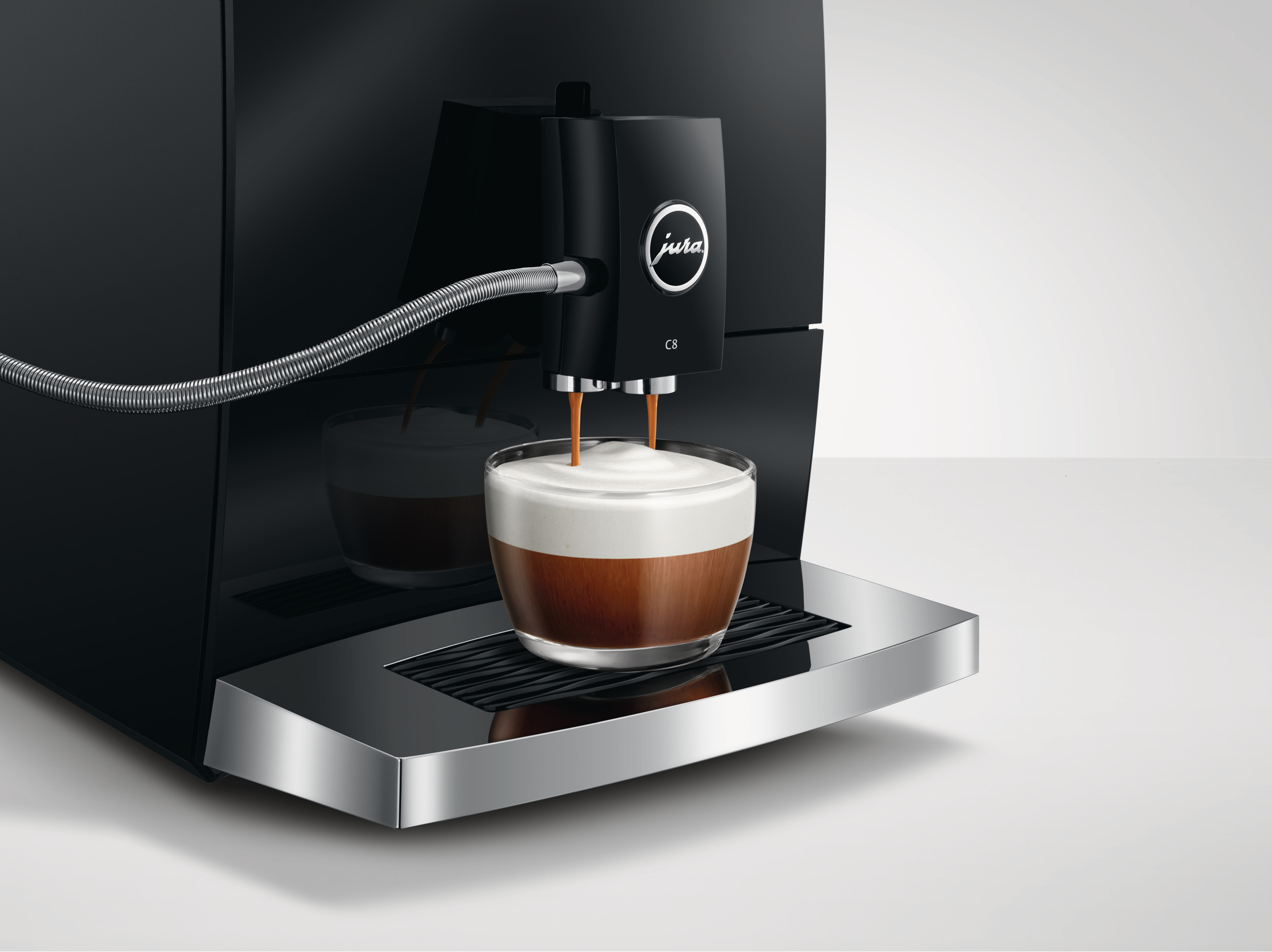 Eine schwarze Jura C8 Kaffeemaschine, die Kaffee in eine Glastasse ausgibt.