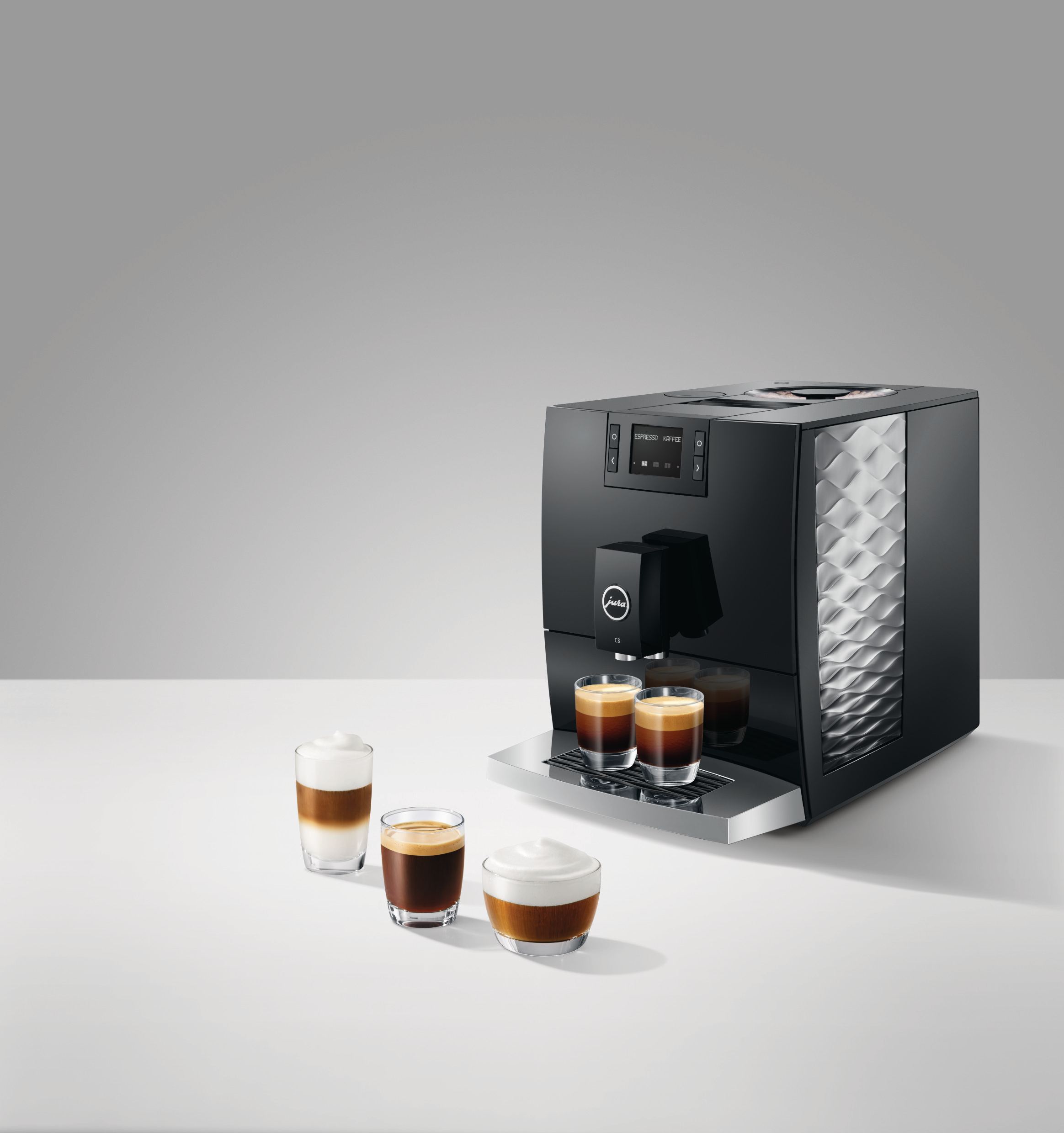 Eine schwarze Jura Kaffeemaschine mit drei Kaffeetassen und einem Milchaufschäumer auf weißer Oberfläche.
