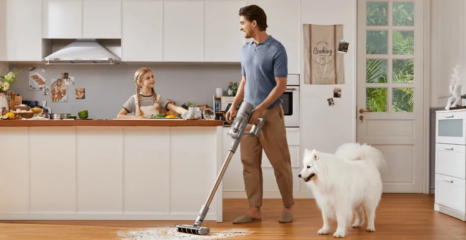 Homme passe l'aspirateur dans la cuisine, fille au comptoir, chien à proximité.