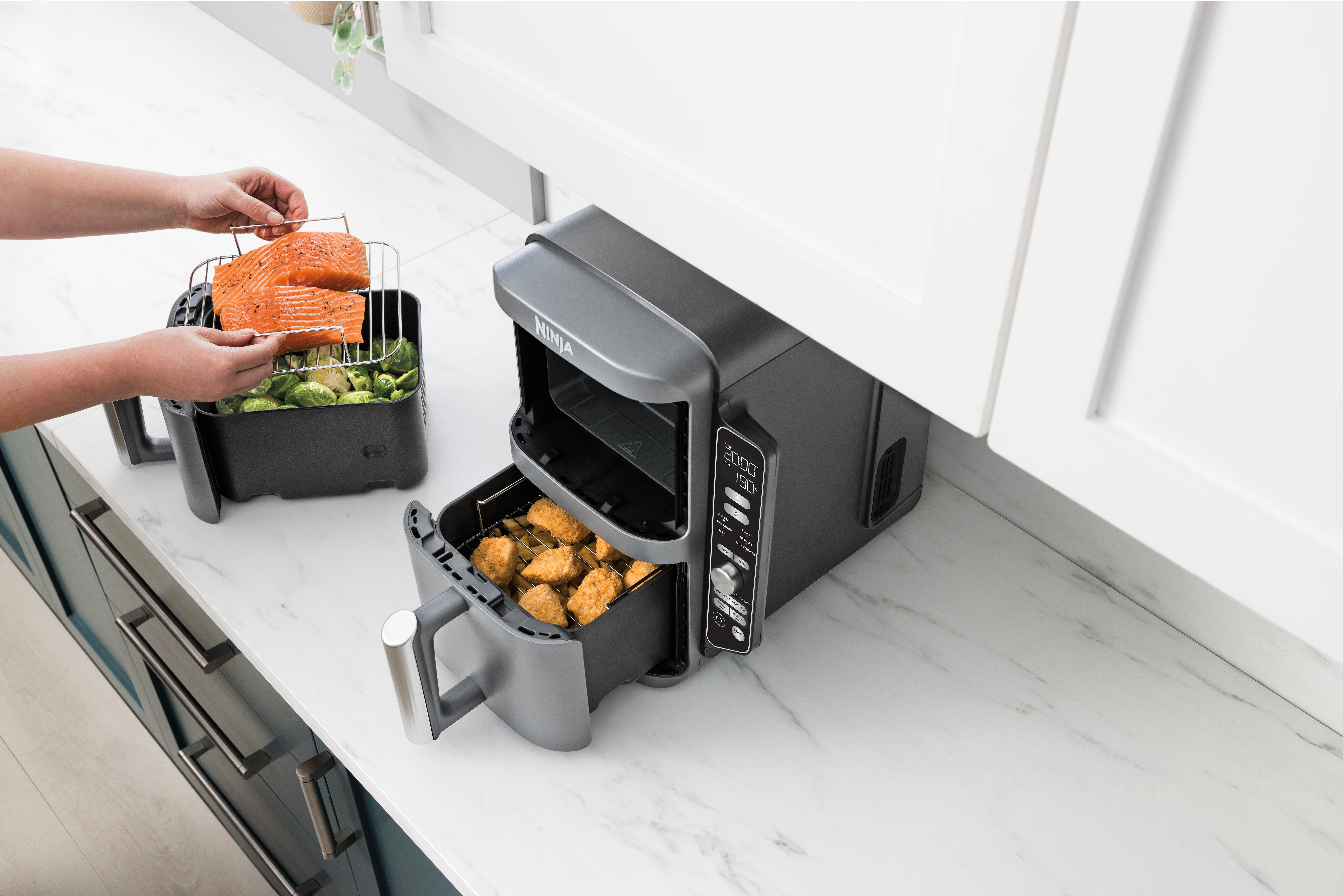 Heißluftfritteuse mit Lachs und Gemüse im Behälter und Frittiertem in der Schublade.
