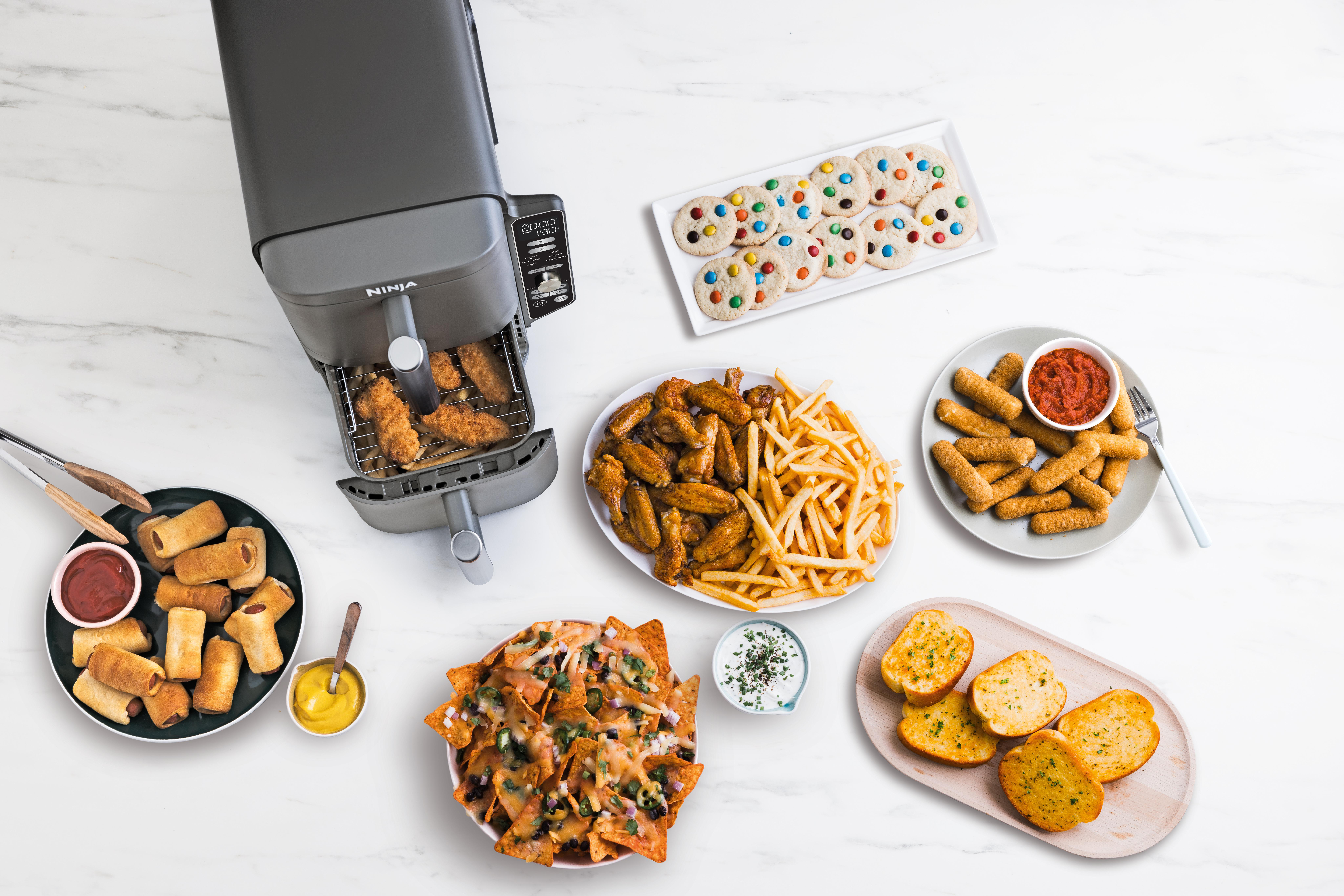 Eine Heißluftfritteuse mit verschiedenen Lebensmitteln: Wings, Pommes, Nachos, Kekse und mehr.