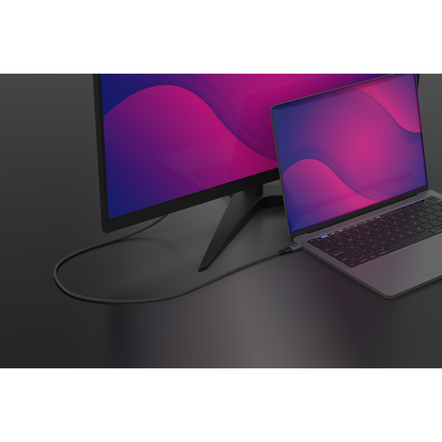 Laptop connected to a monitor via a cable on a black surface. The monitor shows a pink and purple gradient.
