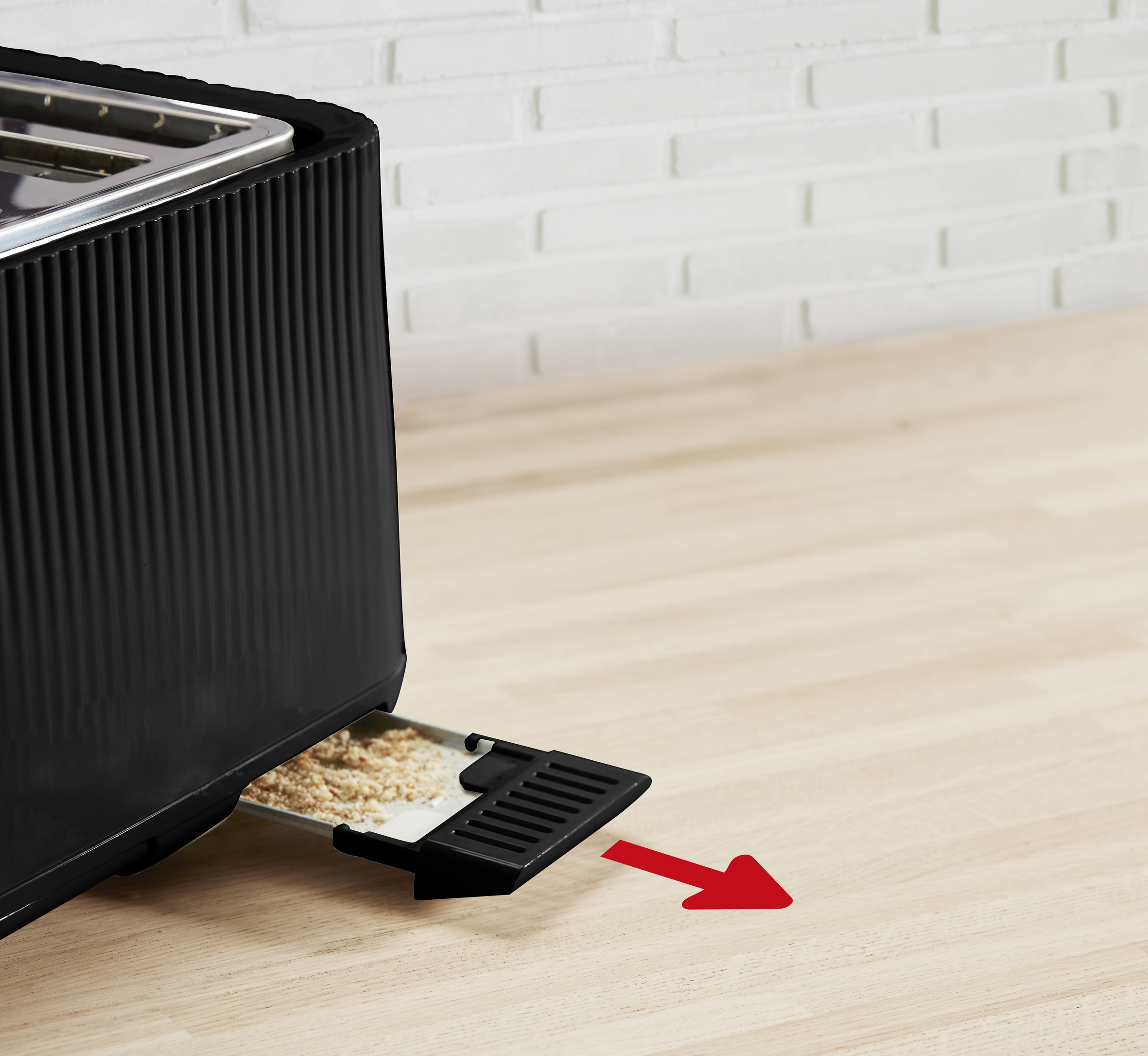 Toster z częściowo wysuniętą tacką na okruchy, strzałka wskazuje kierunek. Drewniana powierzchnia.